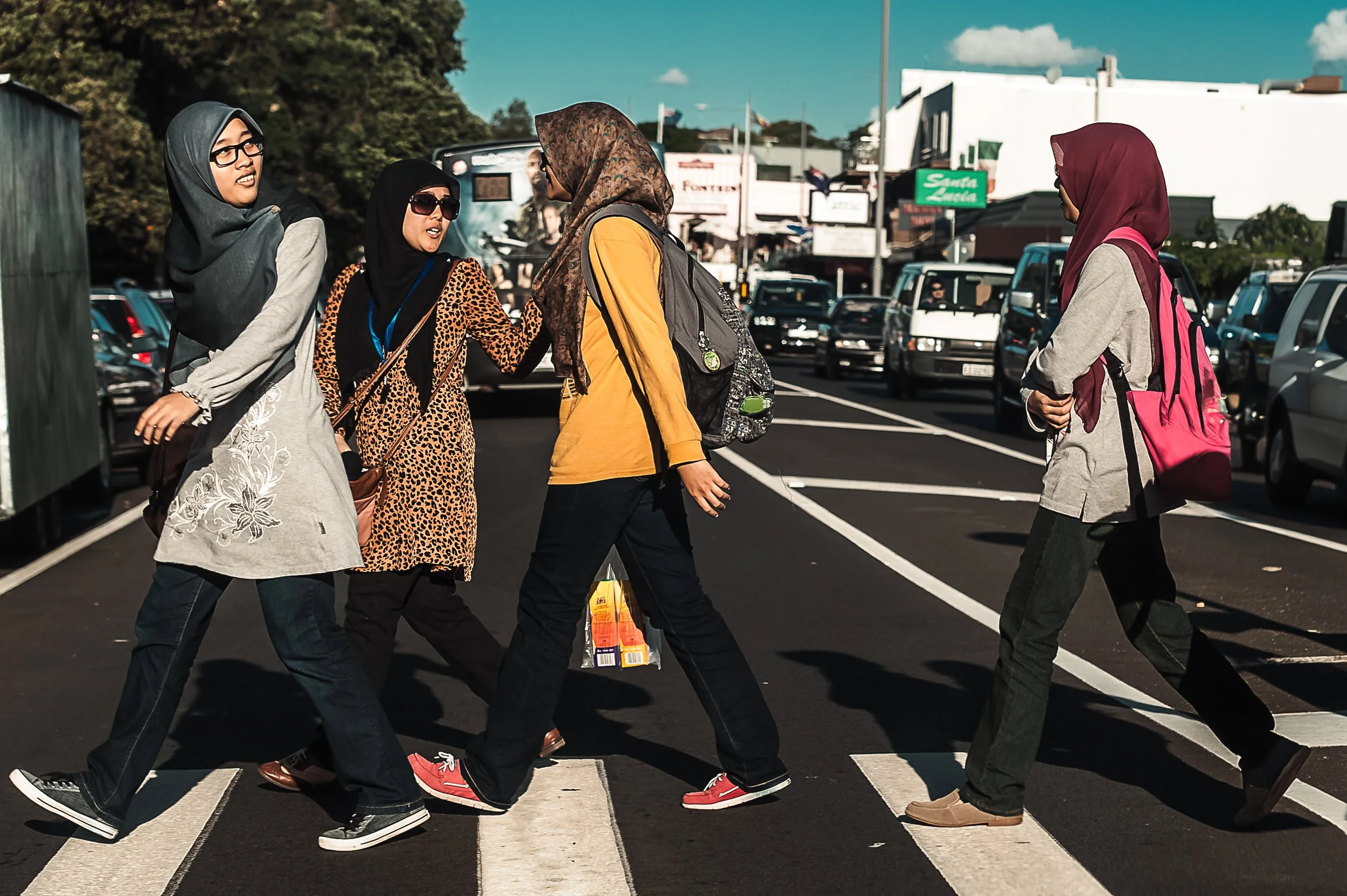 Four women in headscarves walking across a crosswalk with cars in the background.