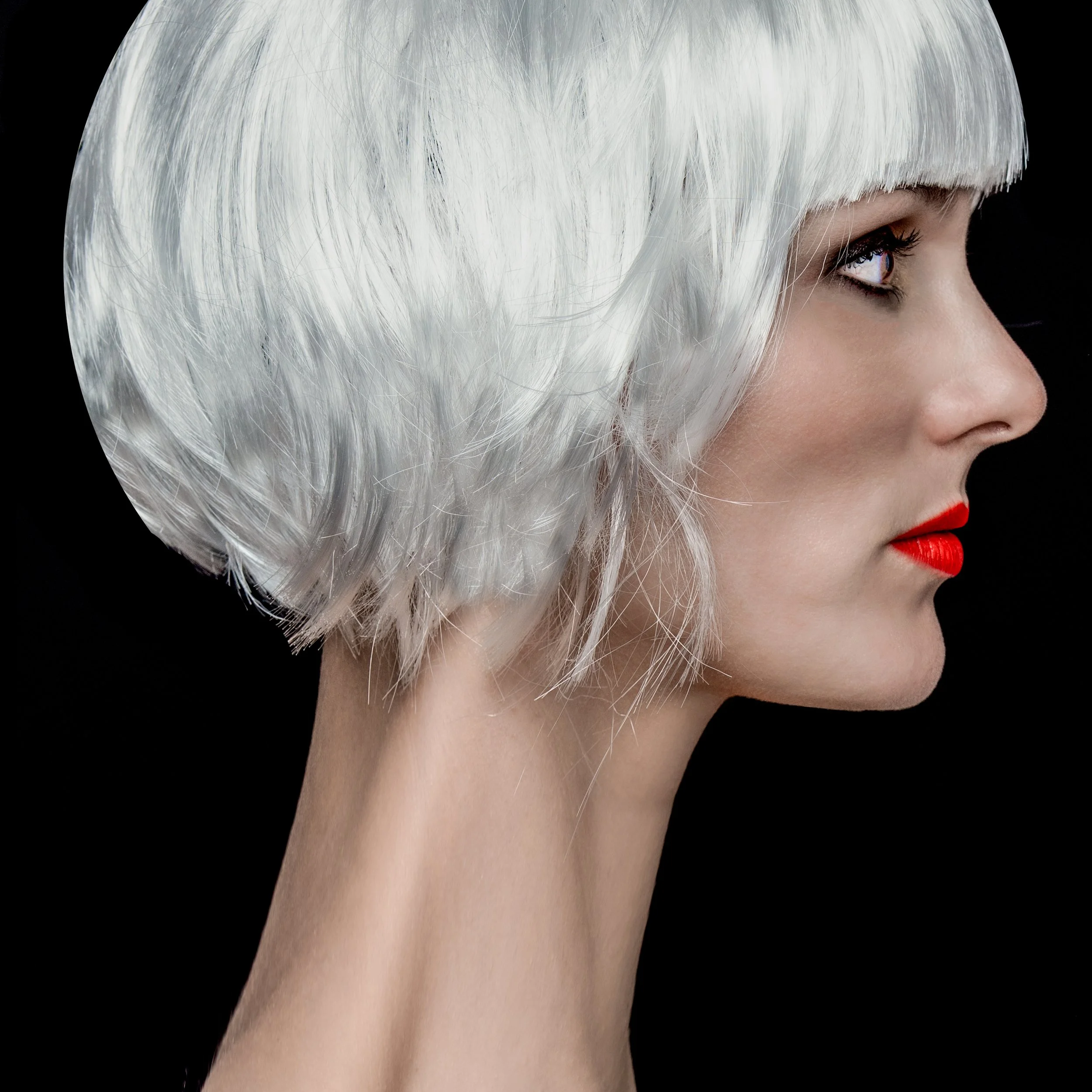 Profile of a woman with a white short bob hairstyle and red lipstick against a black background.