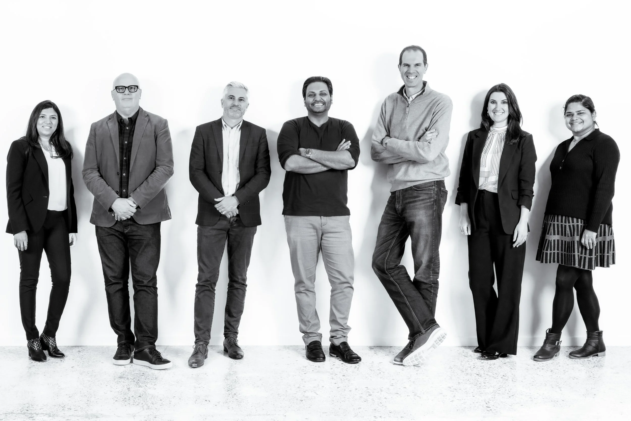 A group of seven people standing against a white background in a professional setting, smiling and casually dressed.