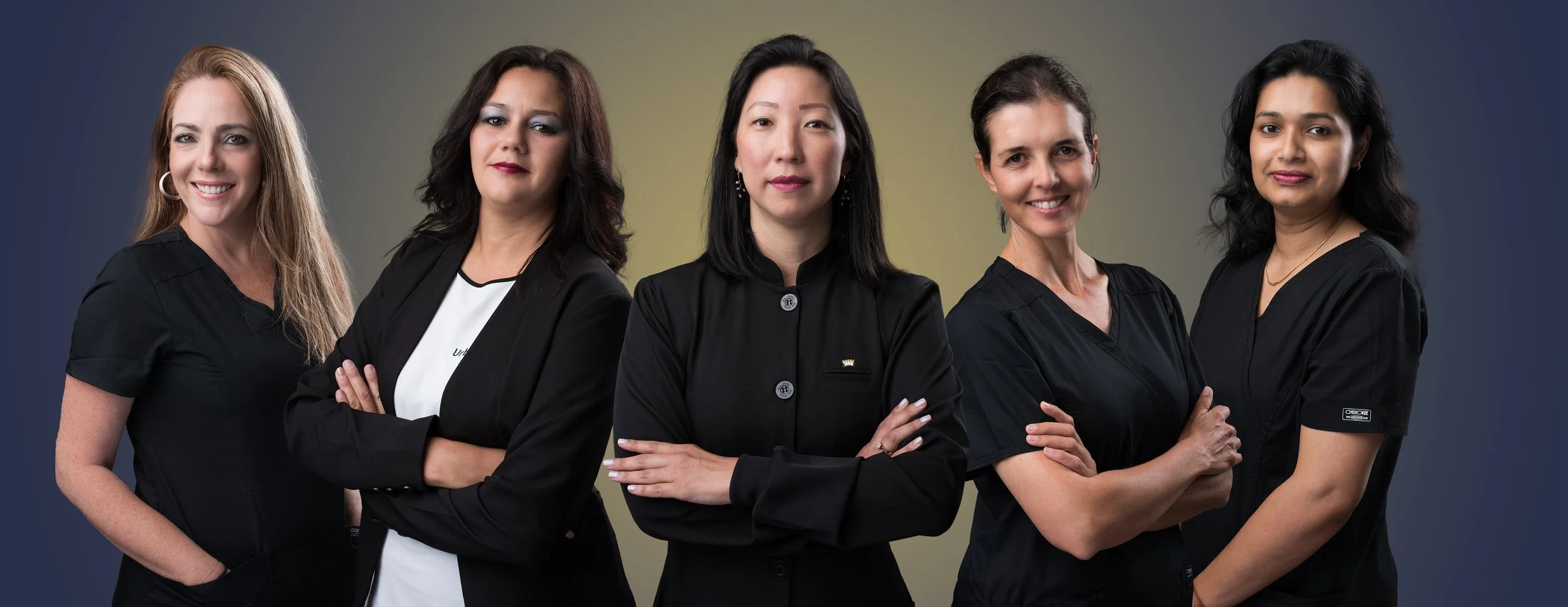 Five women posing confidently, wearing black professional attire, against a gradient background.