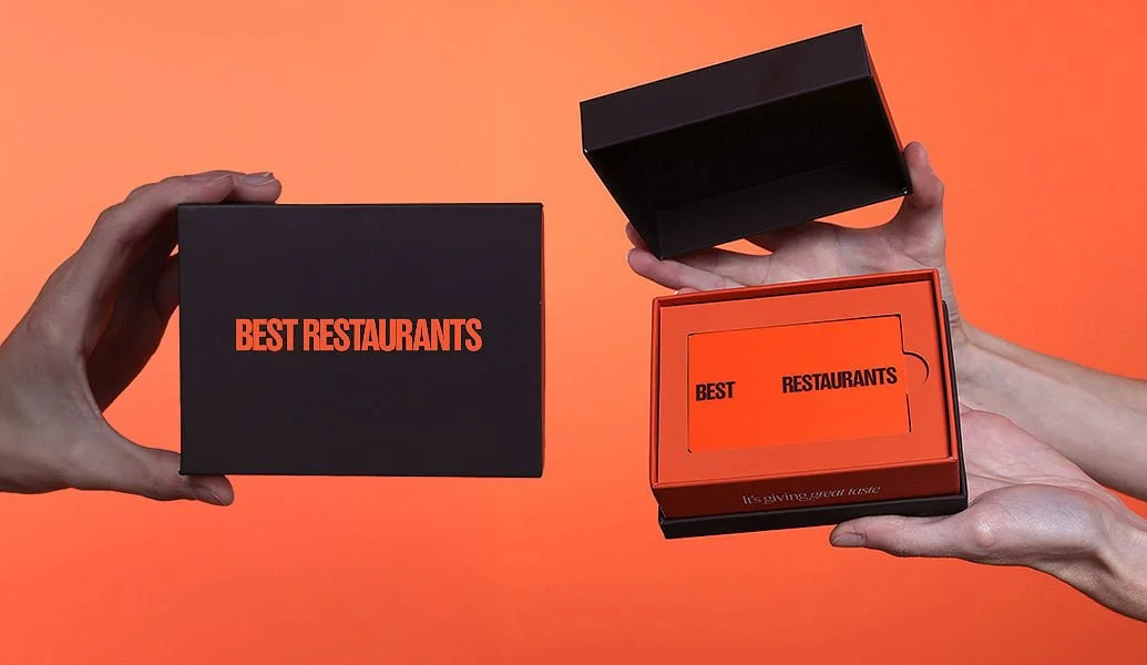 Two hands holding black and orange boxes with the words "Best Restaurants" on them, against an orange background.