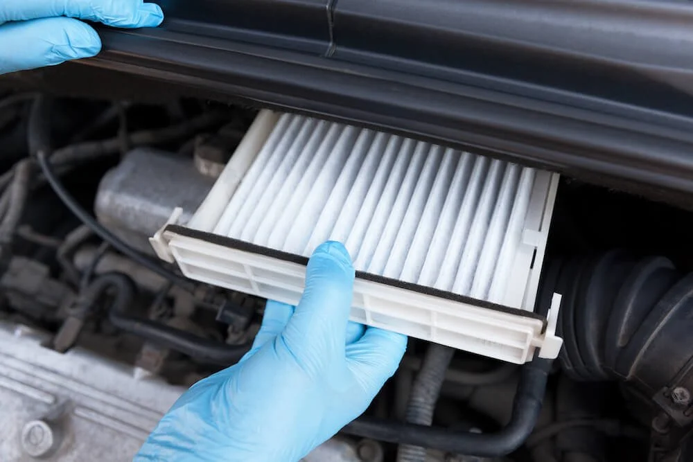 gloved hands replacing an air filter on a car