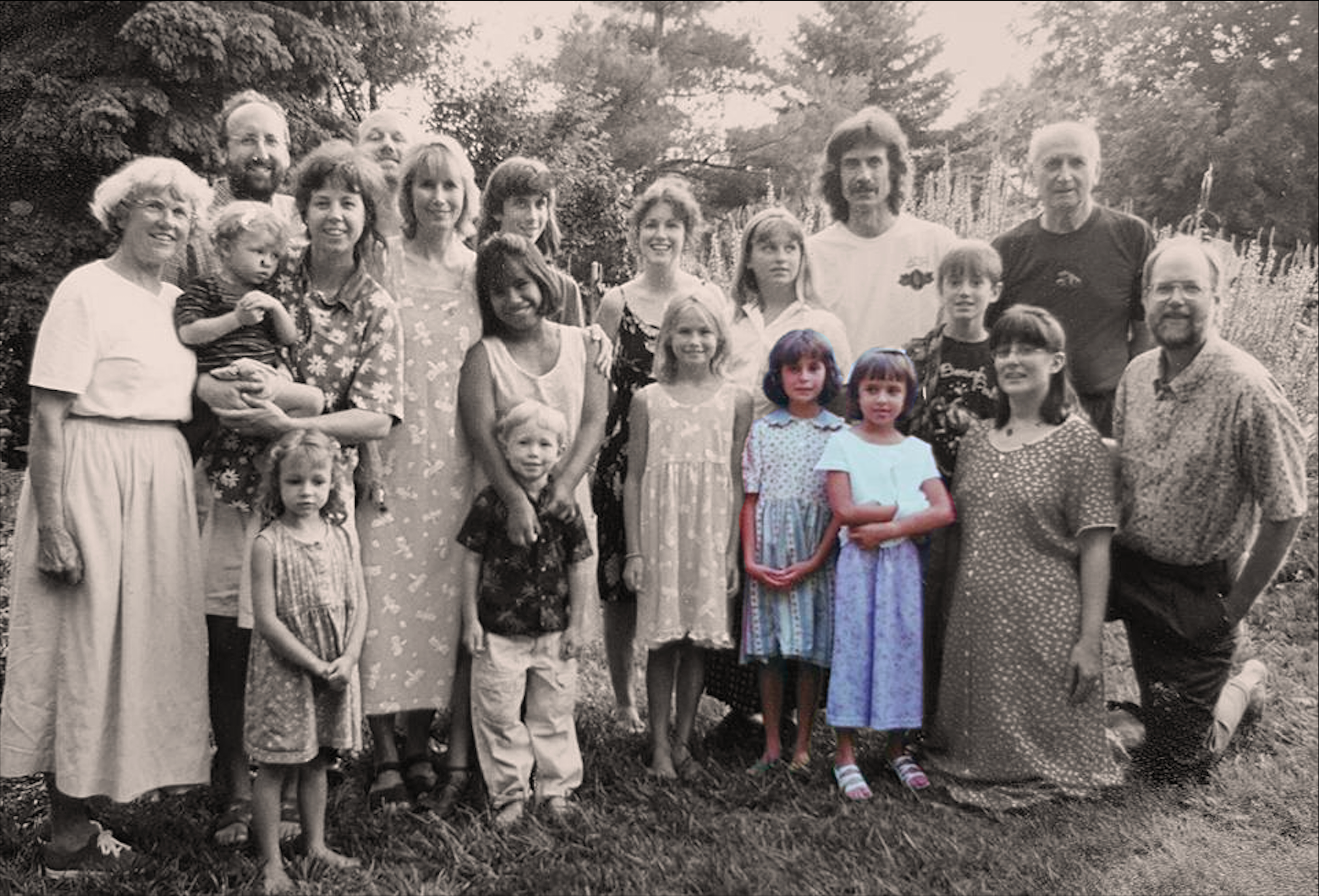 A black and white group photo of multiple generations, including children, adults, and elderly, outdoors in a garden or park setting.