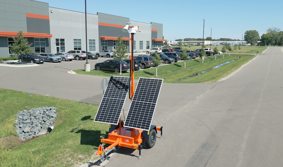 Mobile solar-powered weather station with solar panels and meteorological instruments in a parking lot near a commercial building.