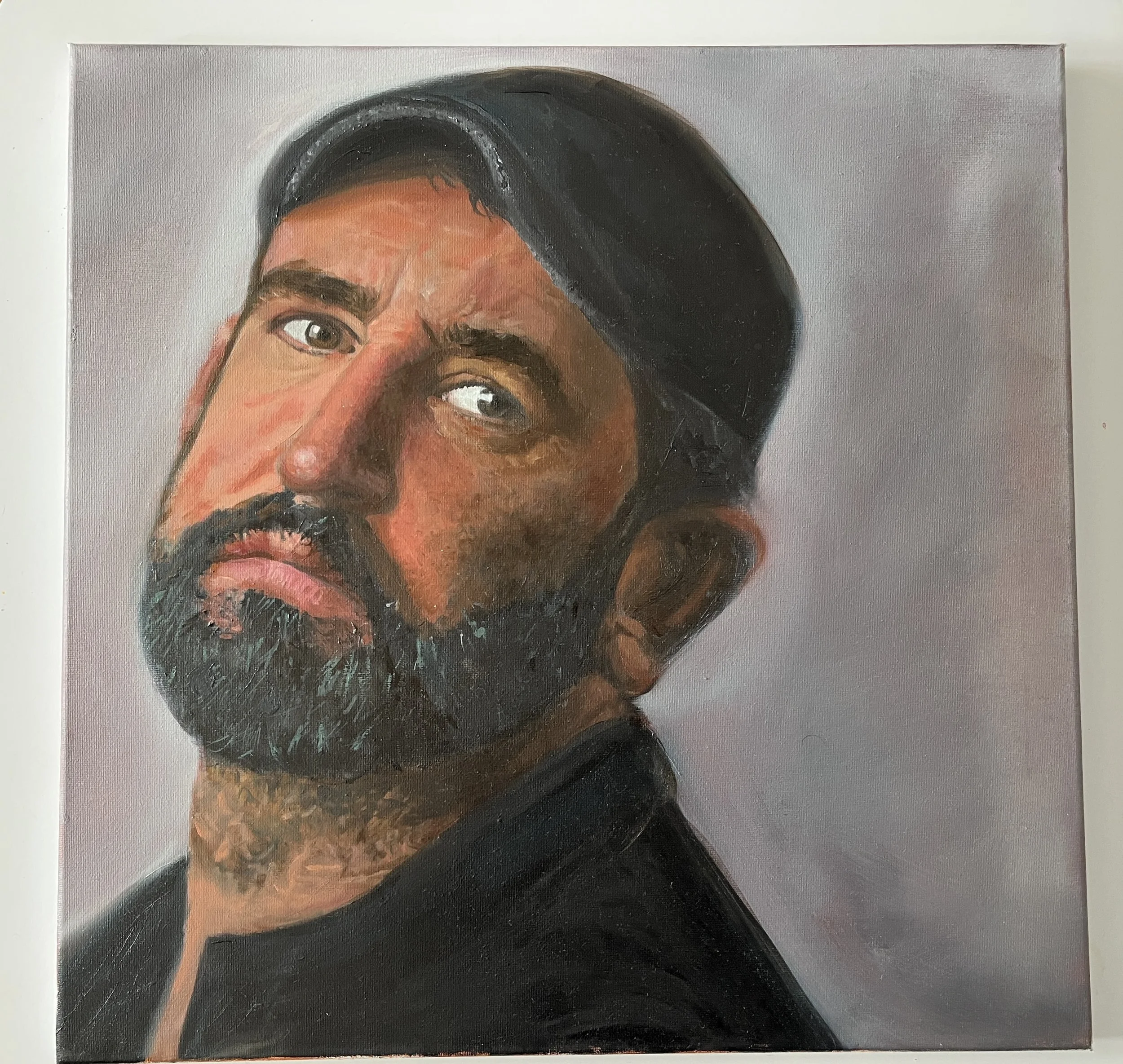 A portrait painting of a man with a full beard, wearing a black cap and black shirt, with a neutral gray background.