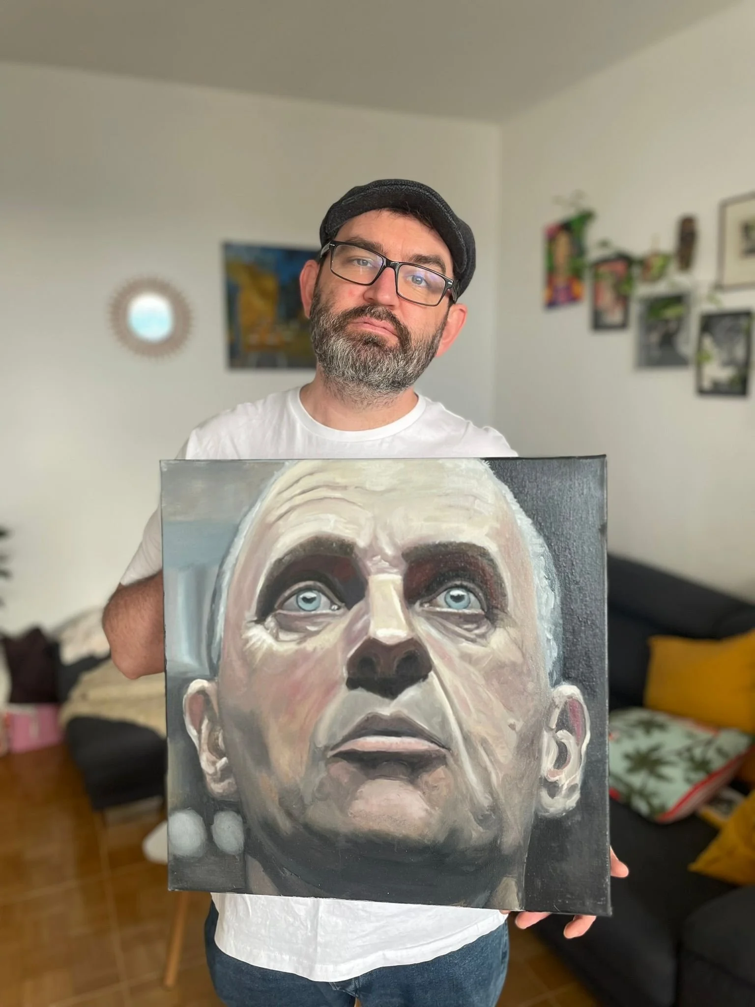 A man with glasses and a beard holding a painting of a woman with blue eyes and white hair.