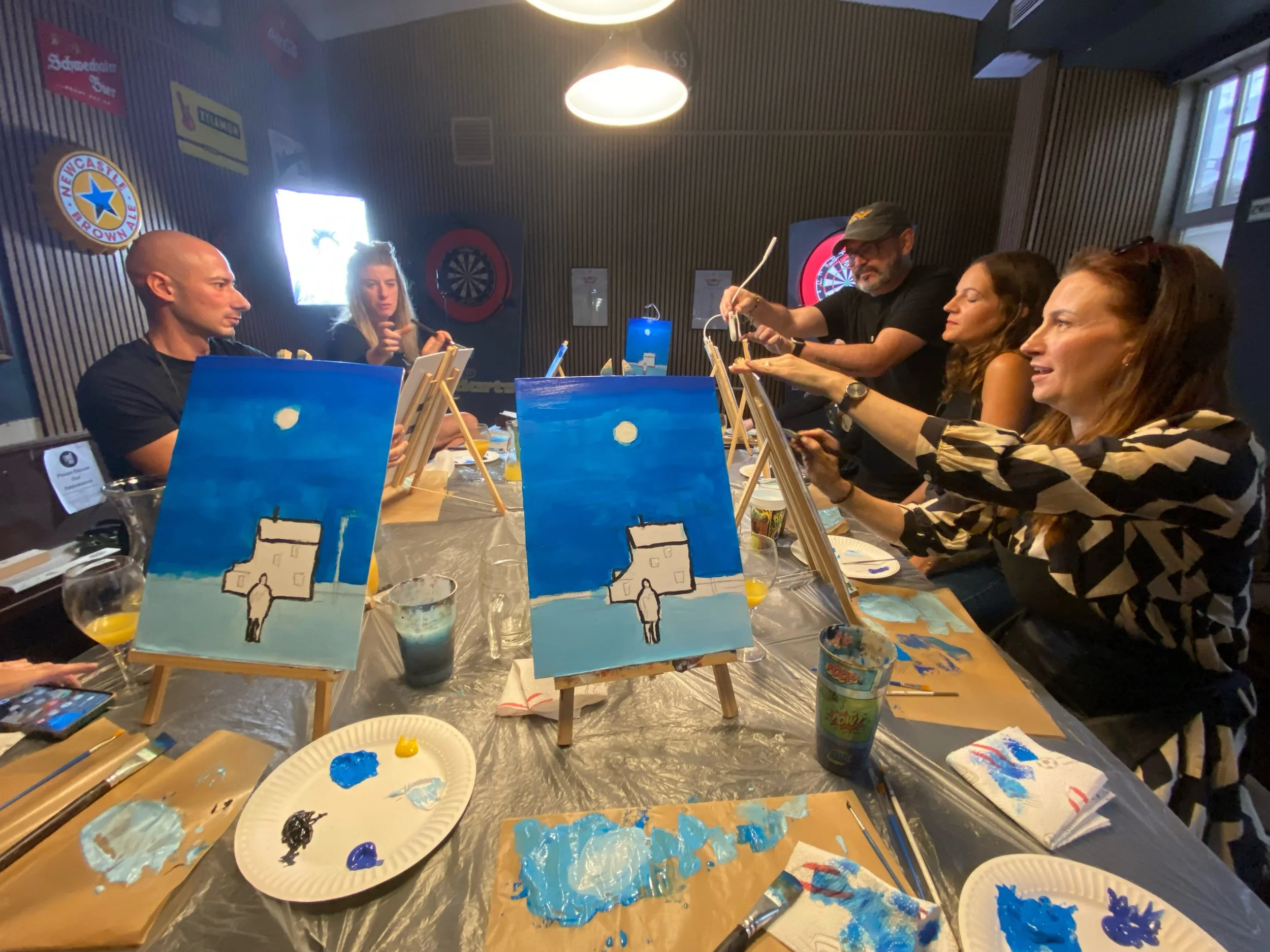 People participating in a group painting class at a long table with art supplies in a room in the Long Hall, Vienna.