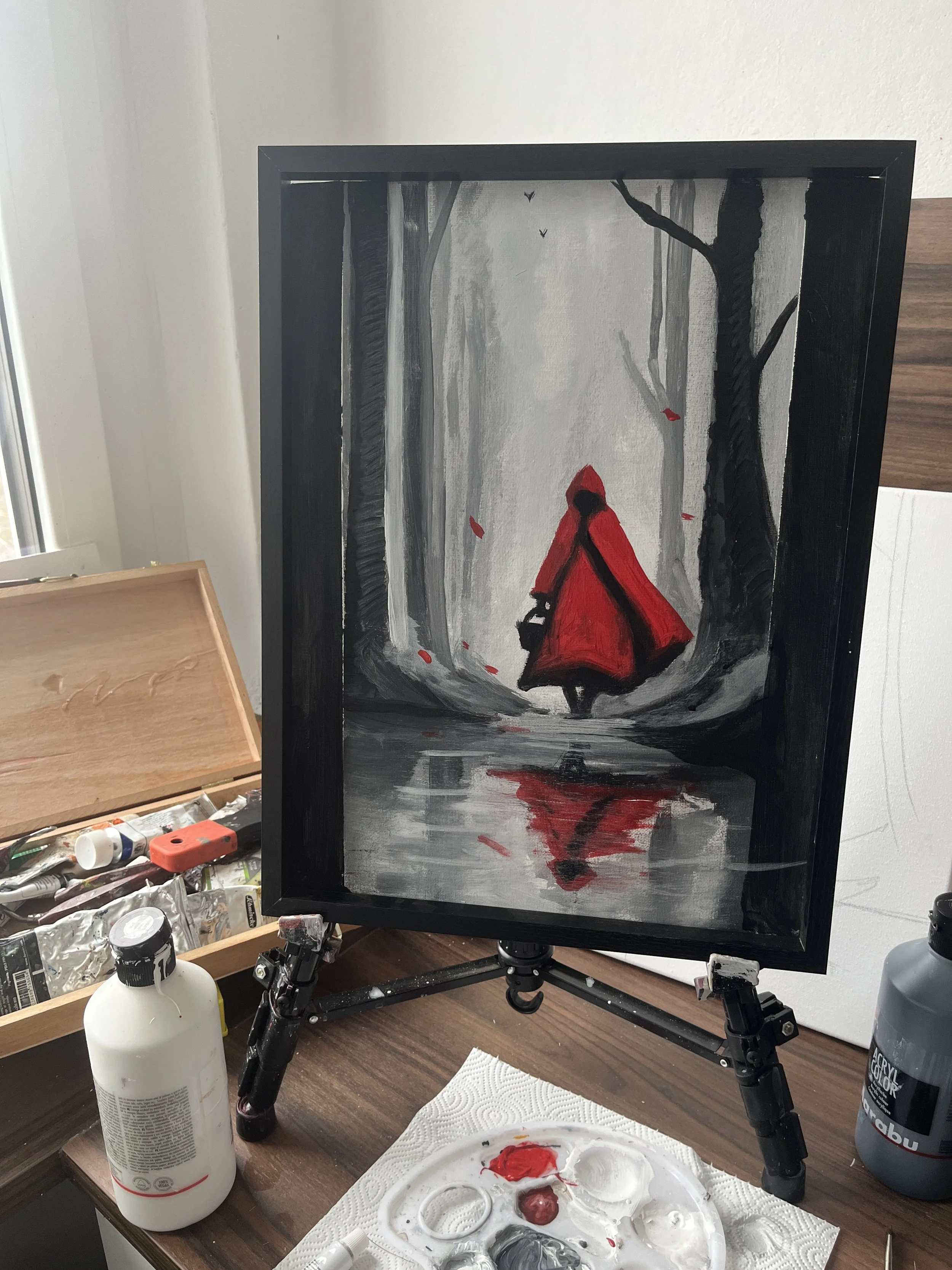 A painting of a person walking through a forest wearing a red hooded cloak, with a reflection of the figure in a puddle on the ground, rendered in black, gray, and red tones.