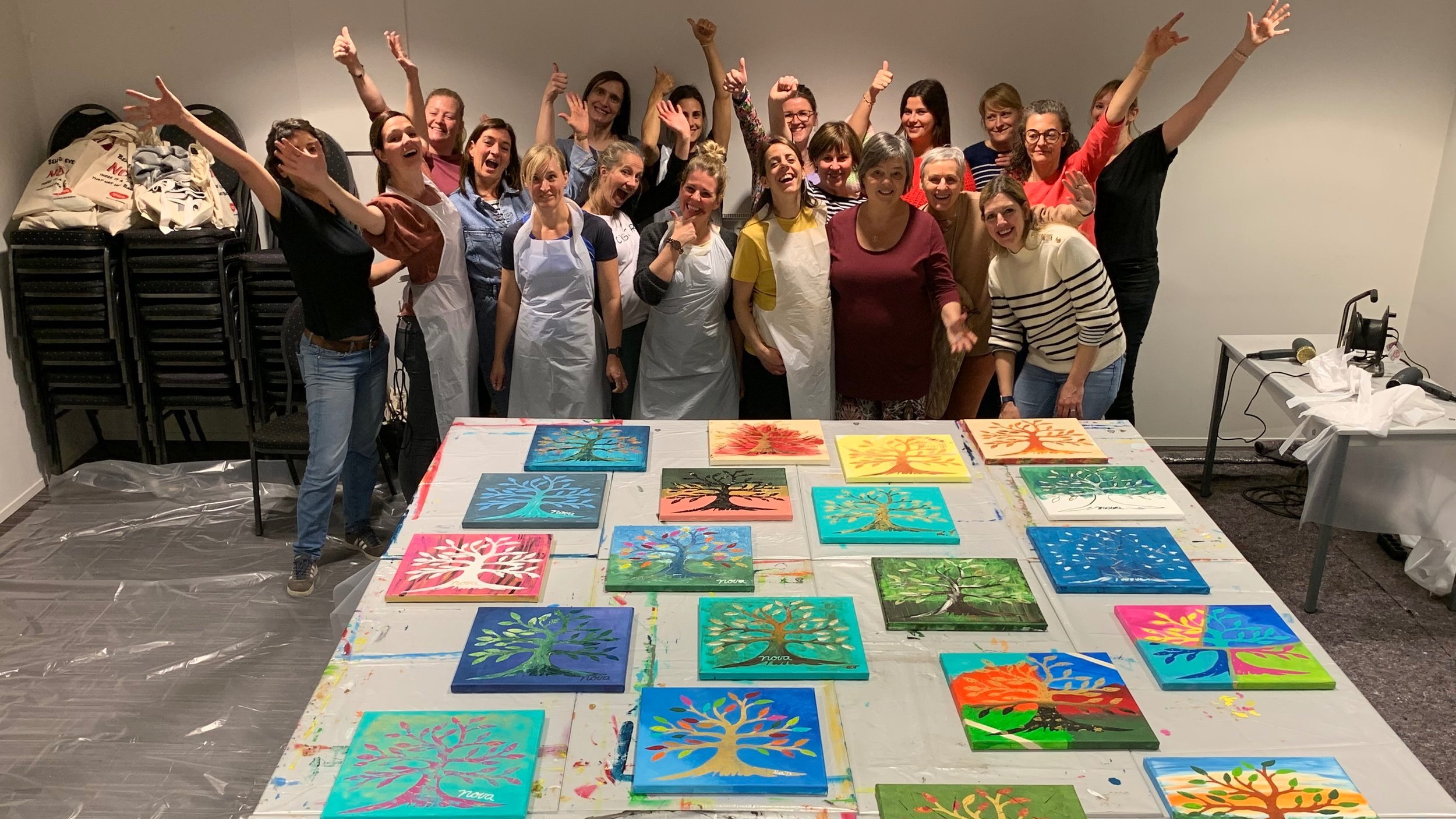 Group of people celebrating around tables with painted tree artwork on canvas.