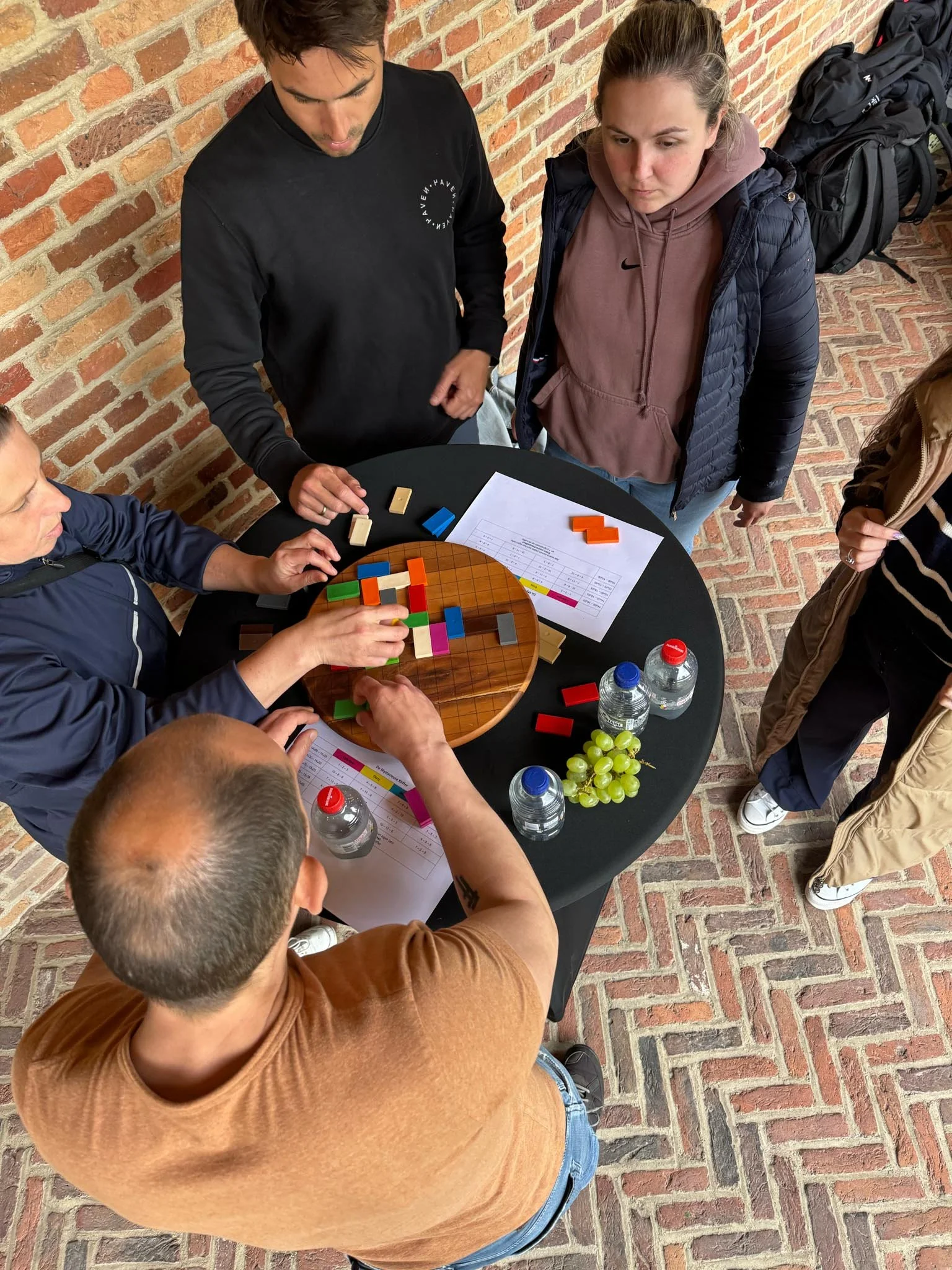 Mensen rond een tafel met een bordspel, gekleurde blokken en flessen water.
