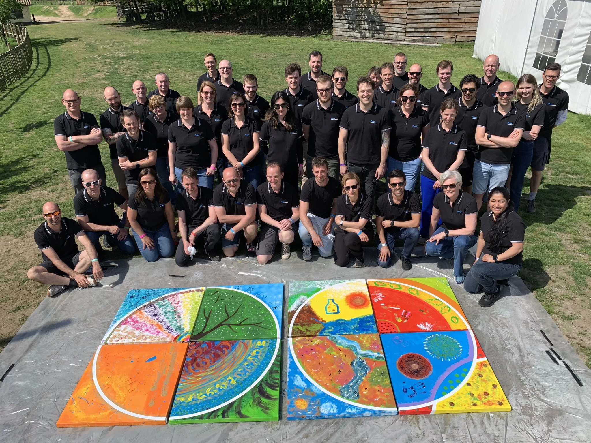 Group of people in black shirts posing outdoors with circular paintings on the ground.