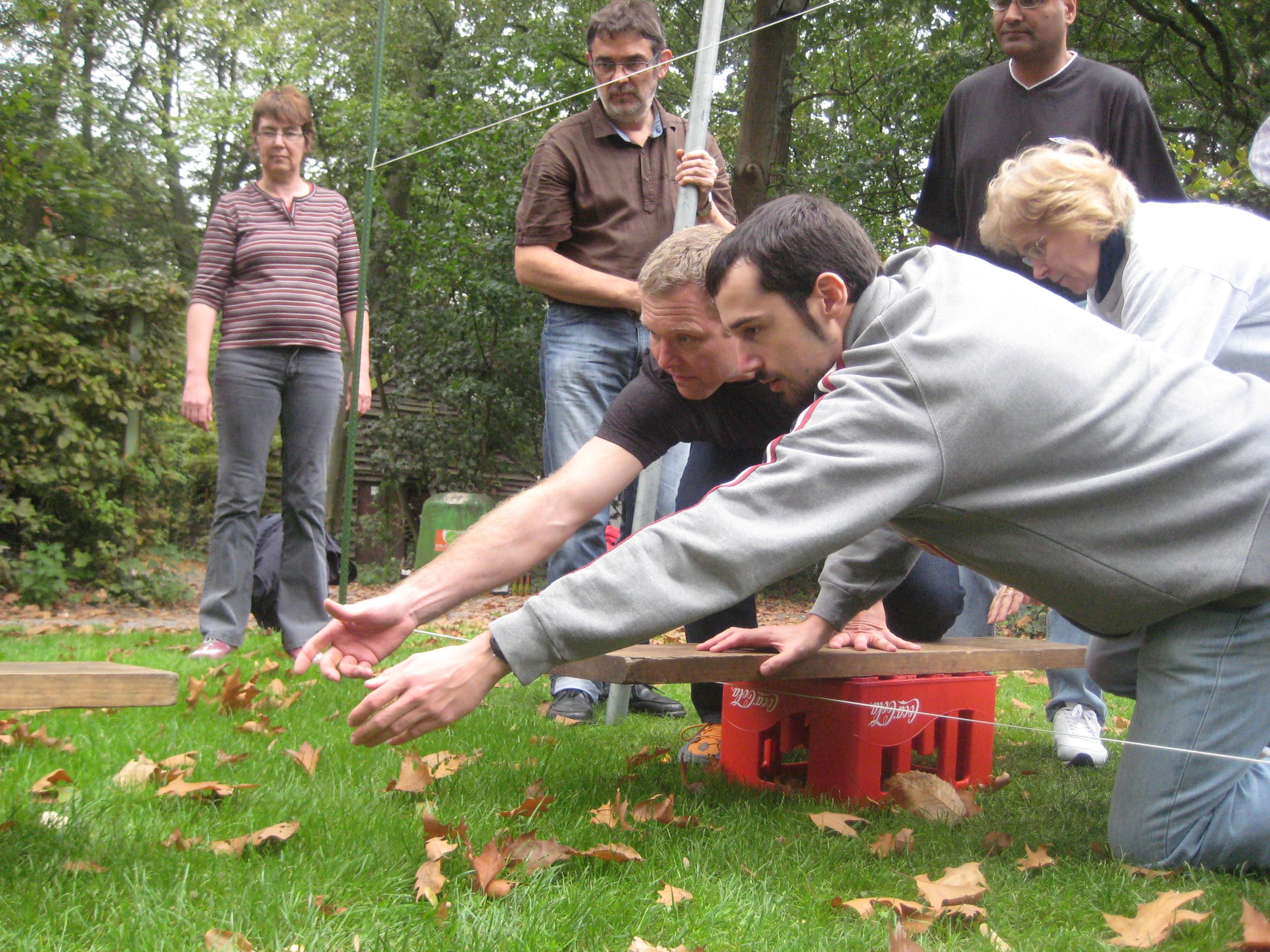 Kinderen spelen in een ondiepe beek terwijl ze proberen over een touw te balanceren in een bosrijke omgeving.