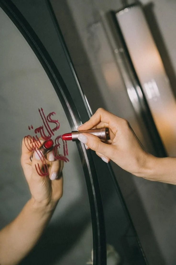 Person writing the word 'Smile' in red on a glass surface with a red marker.