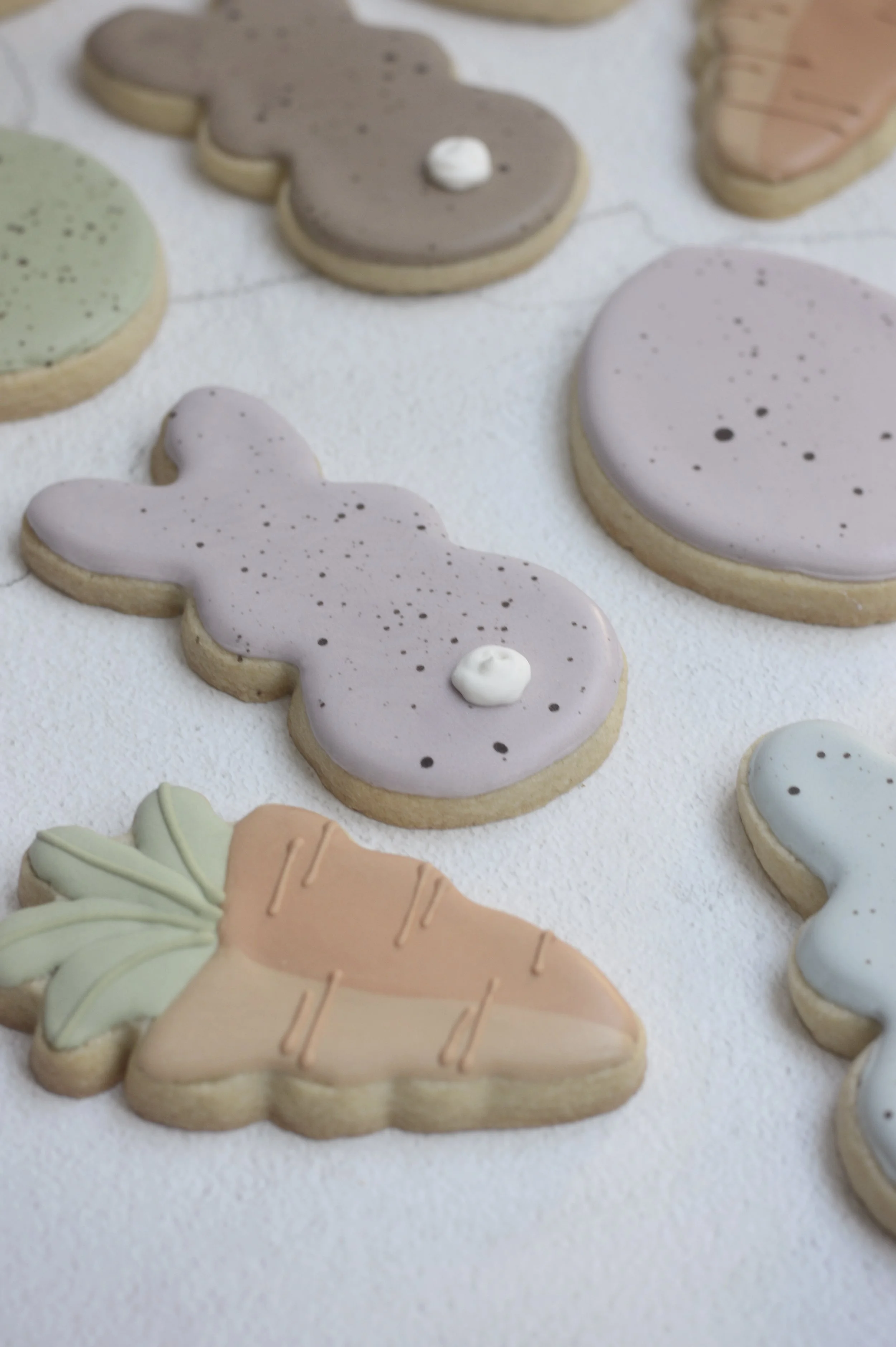 Assorted pastel-colored Easter cookies shaped like bunnies, eggs, and carrots on a white surface.