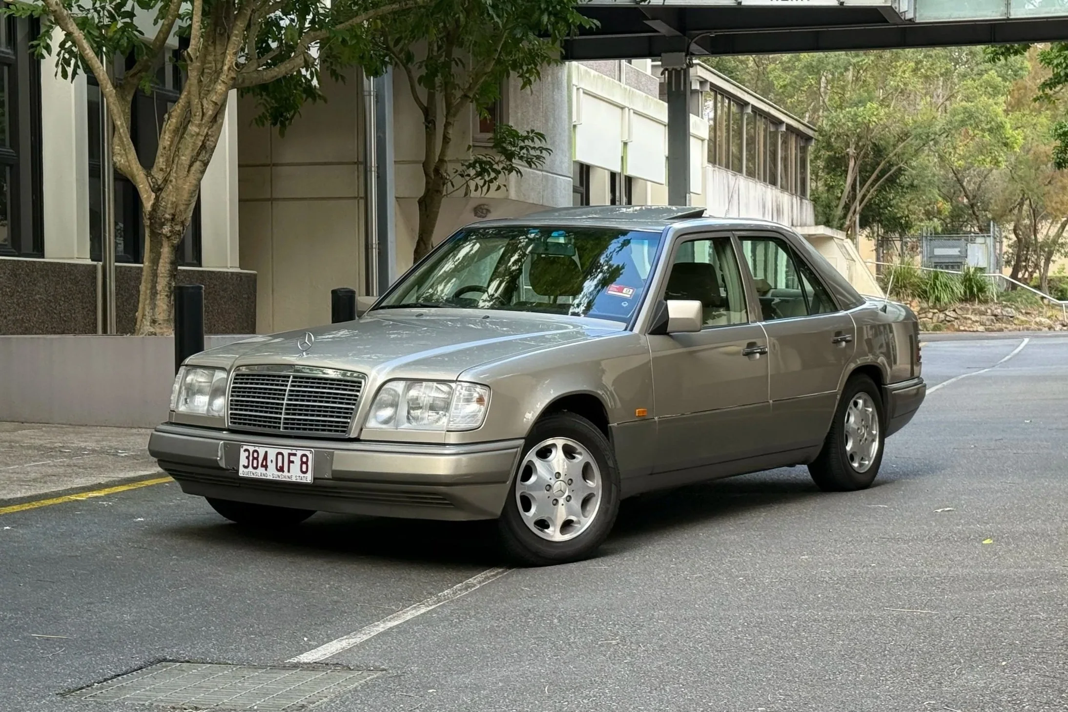 Silver Mercedes-Benz sedan parked in a parking lot with trees and modern building in the background.