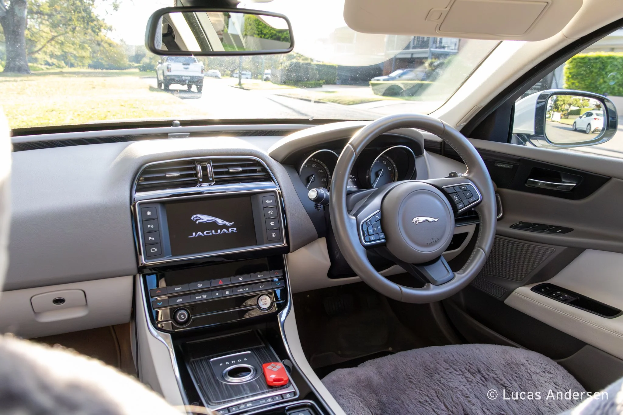 Interior of a Jaguar car showing the dashboard, steering wheel, and center console, with a view of the street through the windshield and side mirrors.