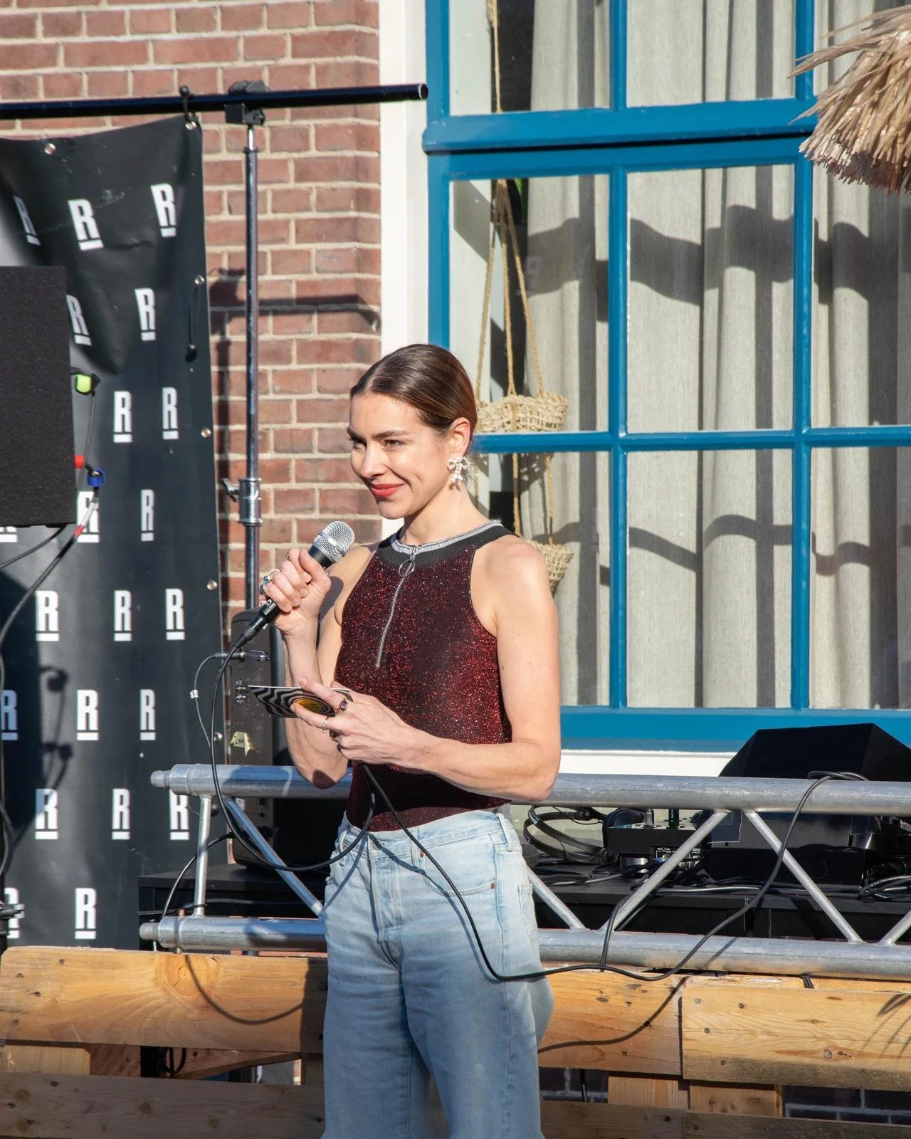 Vrouw die op een podium staat, met een microfoon in haar hand, tijdens een buitenoptreden. Docent bij Skill School