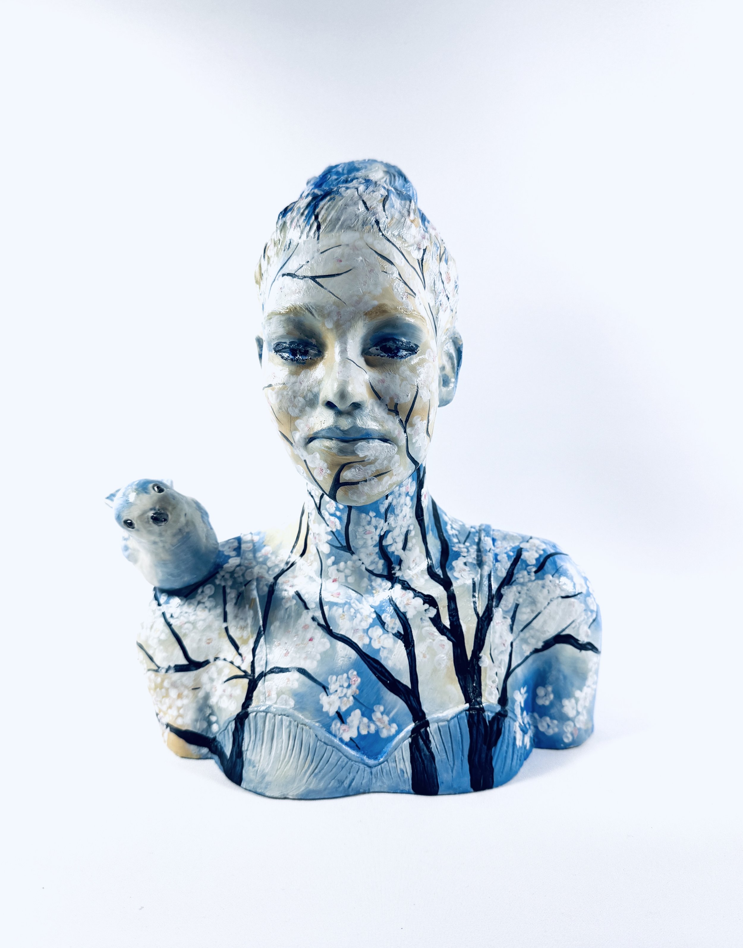 A ceramic sculpture of a female head with a blue bird pirched on her shoulder. 