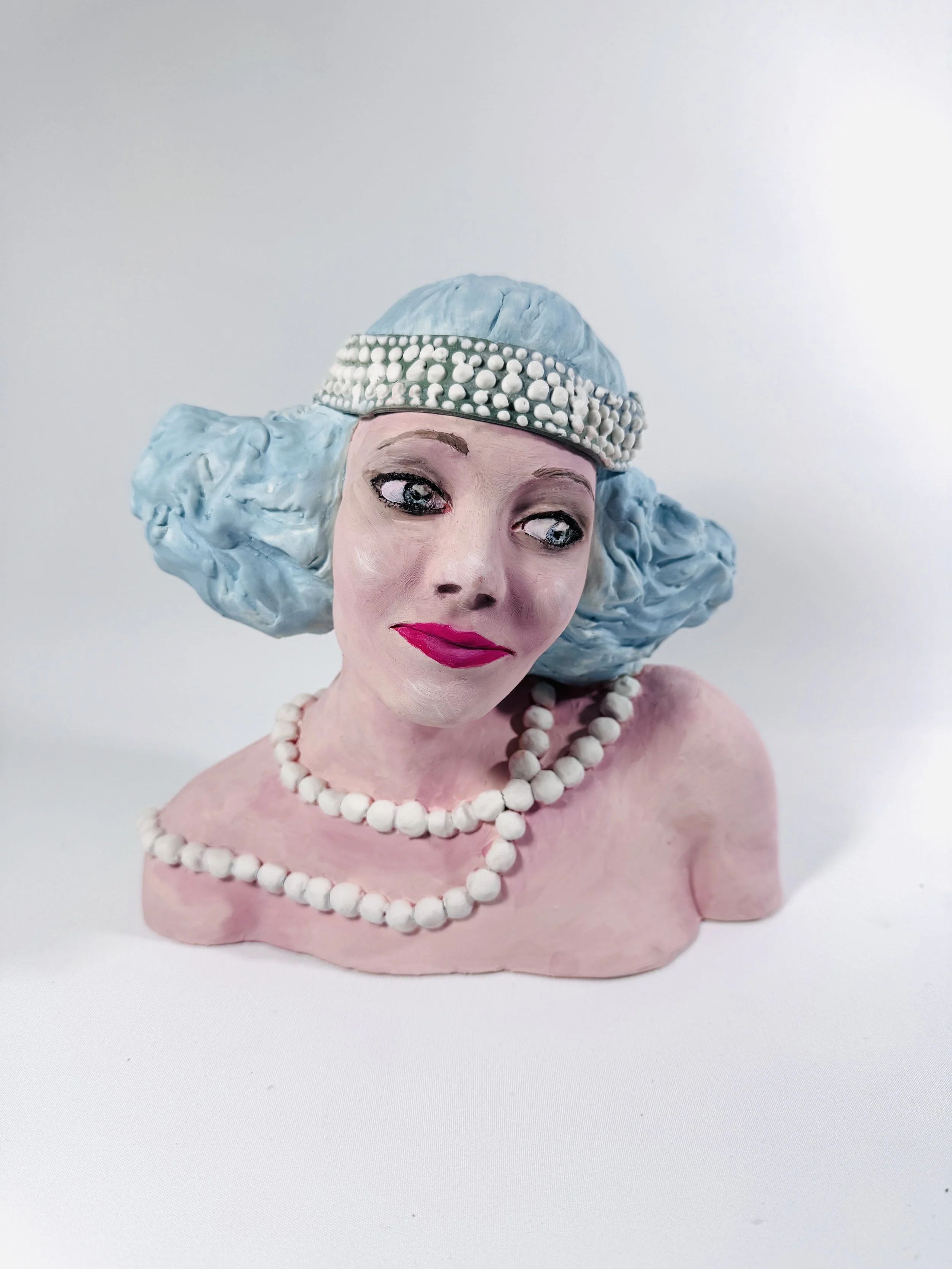 A bust sculpture of a retro style woman with pink skin, blue hair, and wearing pearl jewelry, set against a plain white background.