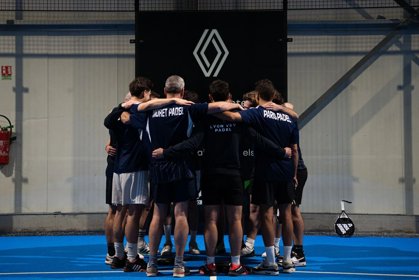 Groupe de joueurs de padel en cercle, en train de s'encourager avant un match sur un terrain de padel.