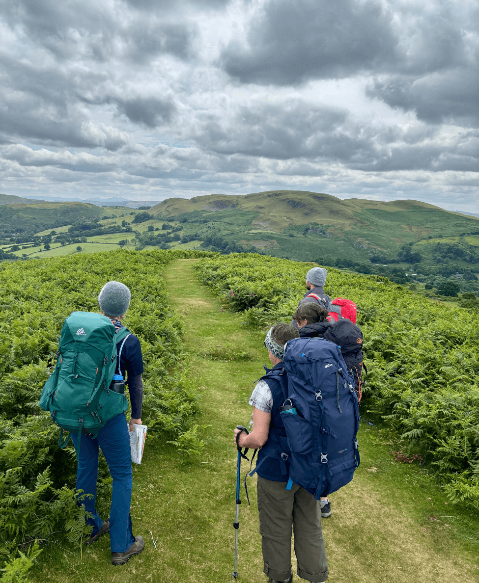 4 people on their wilderness expedition looking out over the welsh hills and admiring the beautiful view.