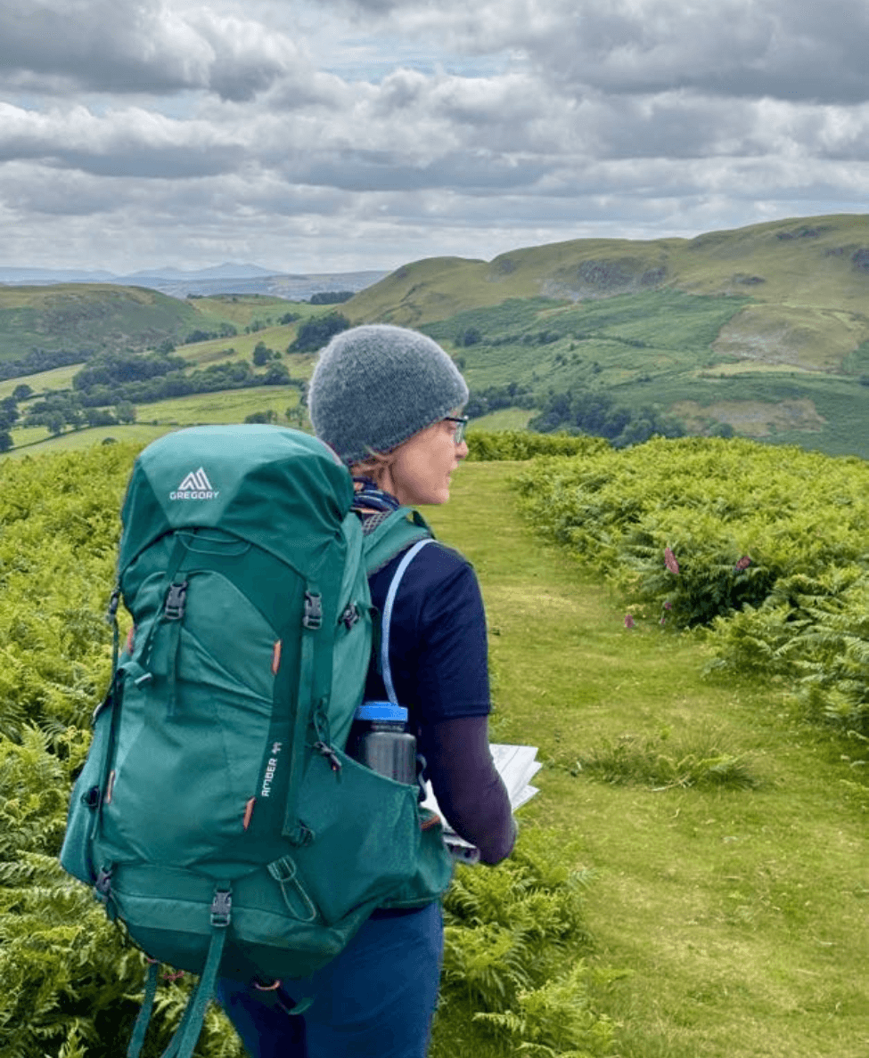 A lady wearing a large expedition rucksack and holding a map on a hiking expedition.
