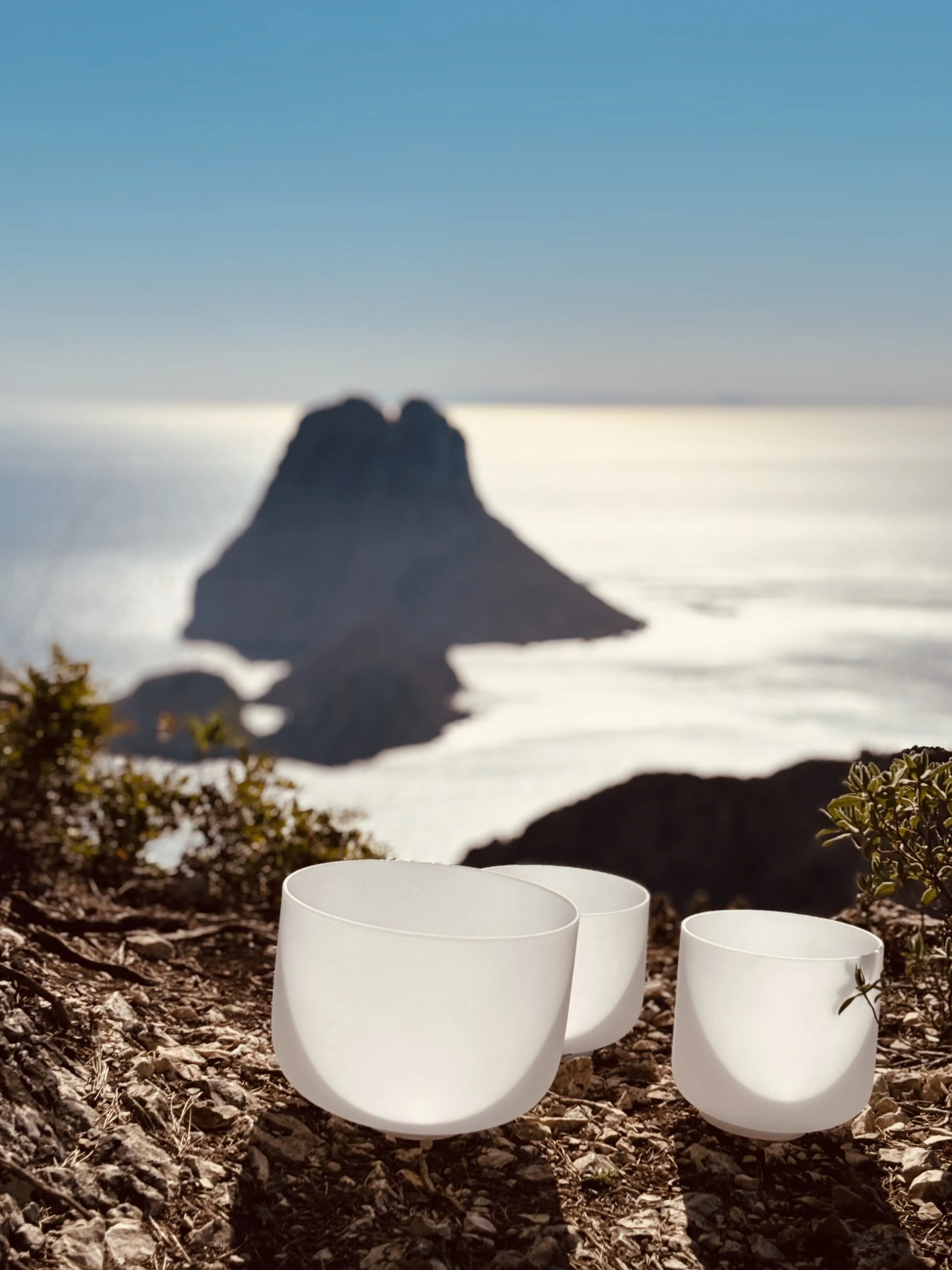 Crystal singing bowls on a clifftop with the island of Es Vedrà in the background