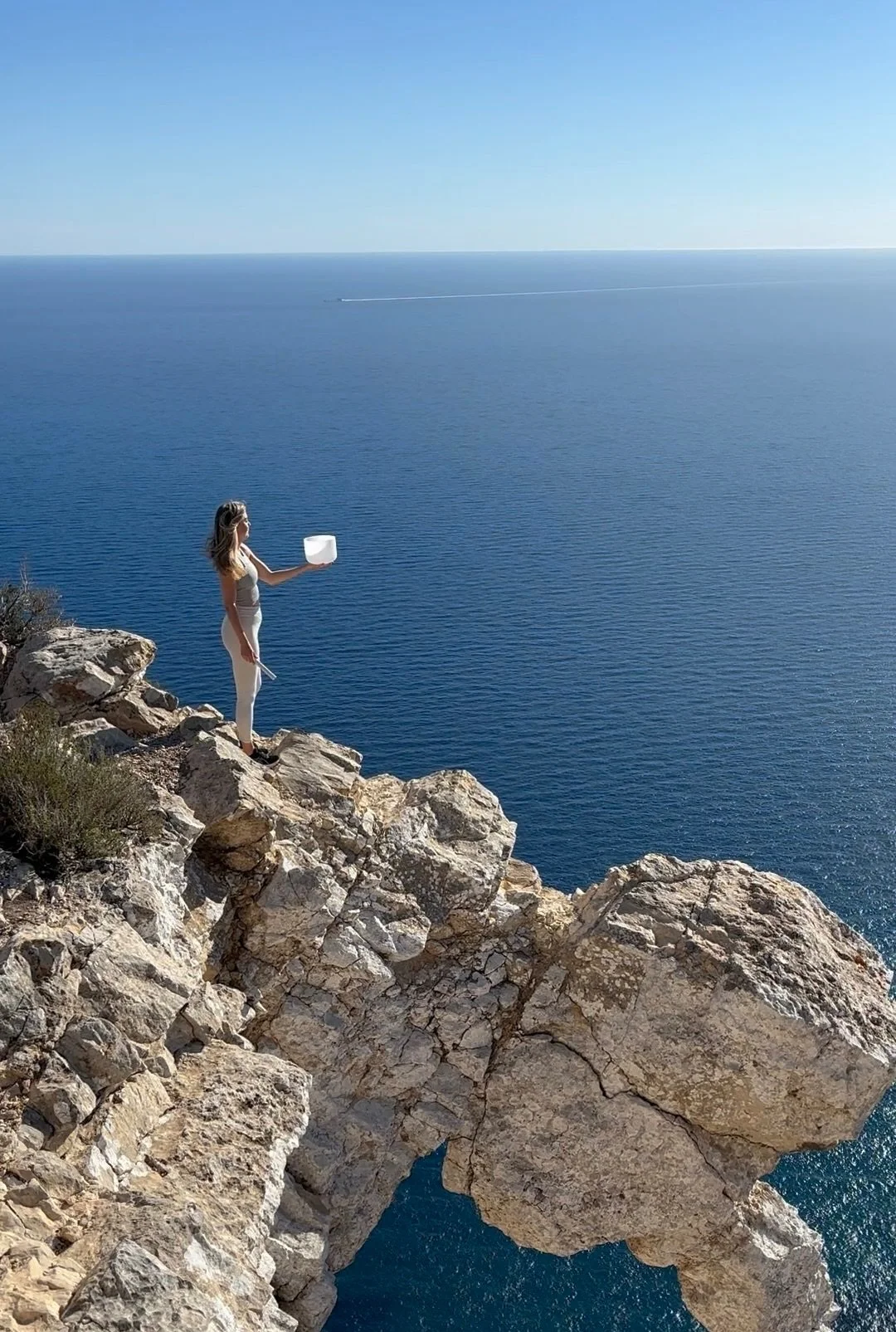 Olivia Pauline holding a crystal singing bowl on a sea cliff at Atlantis, Ibiza