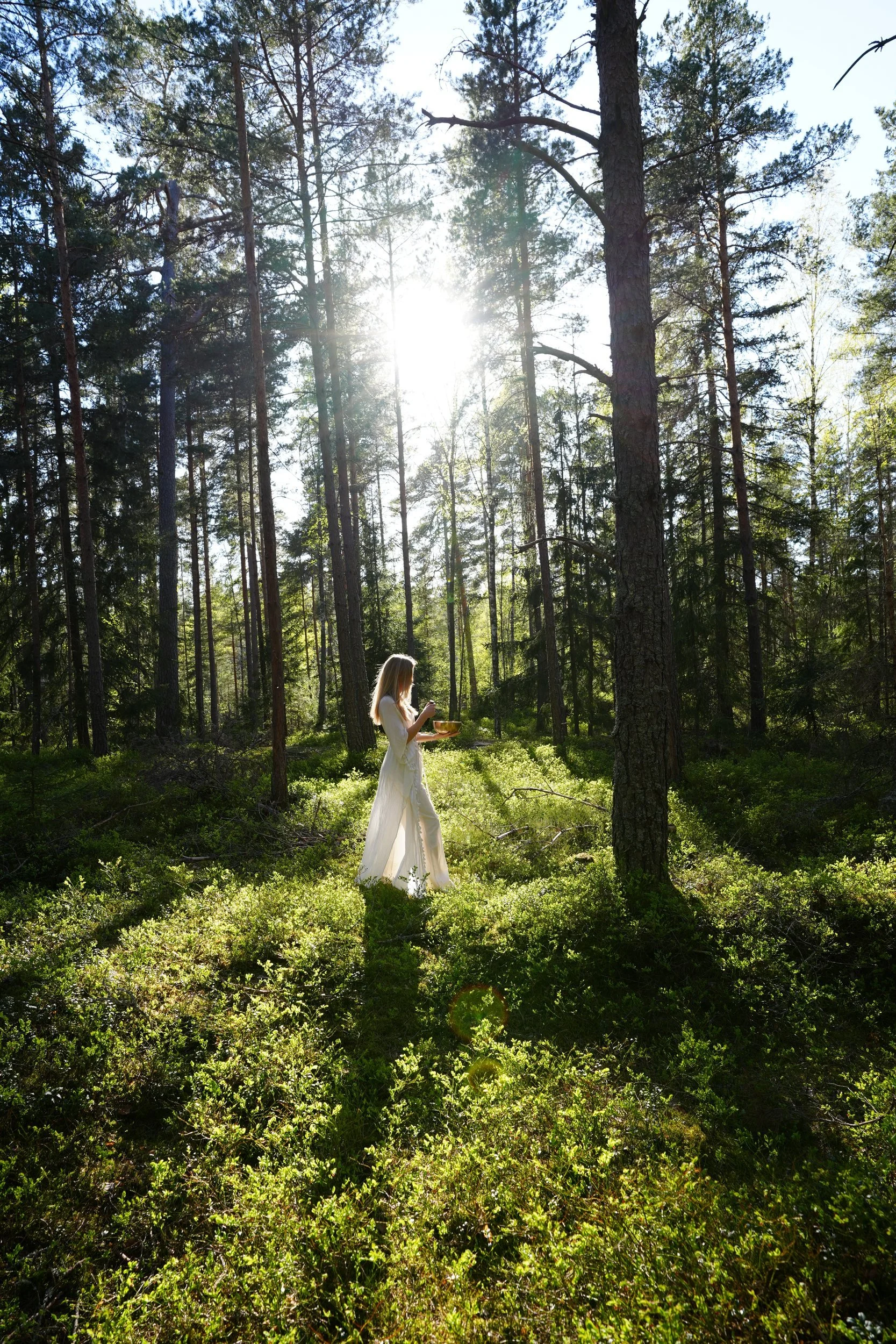 Olivia Pauline walking with a singing bowl through a sunlit pine forest