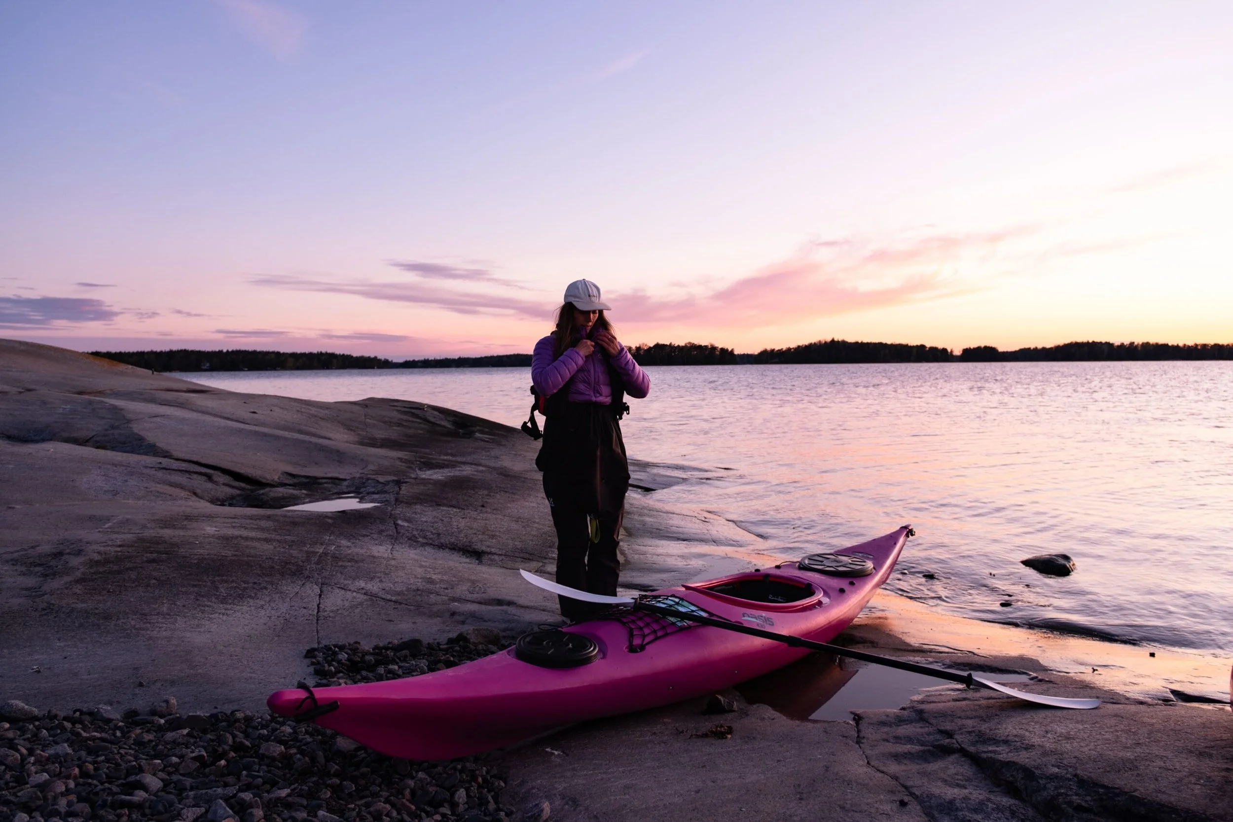Kajakki ja meloja rantakalliolla auringonlaskussa