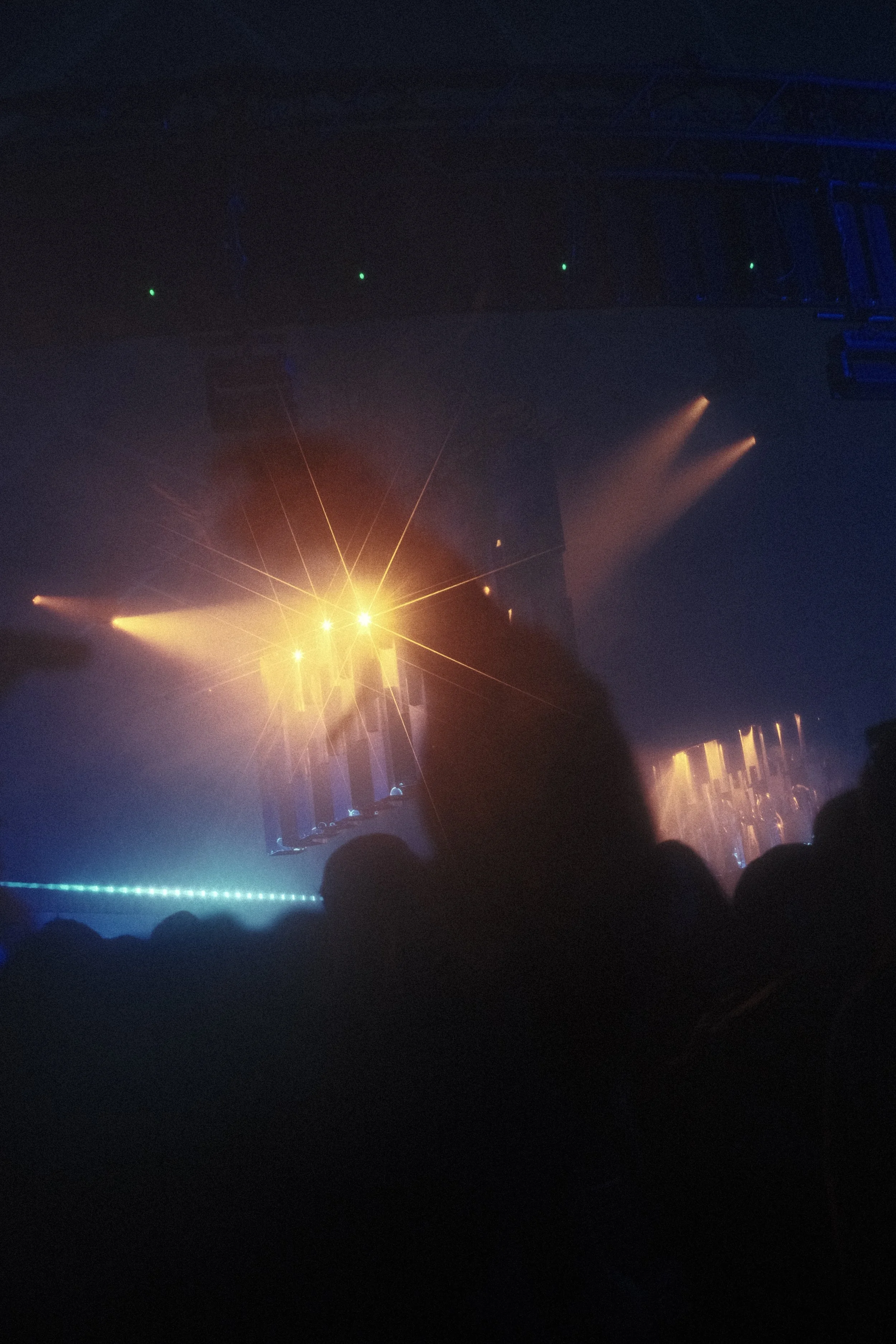 Dark concert scene with stage lights and fog, silhouette of an audience, and people or performers faintly visible in front of the stage. Reflecting Bodies VI Voodoo Village Belgium Scenography art installation light installation Simone Smelt Lumus In