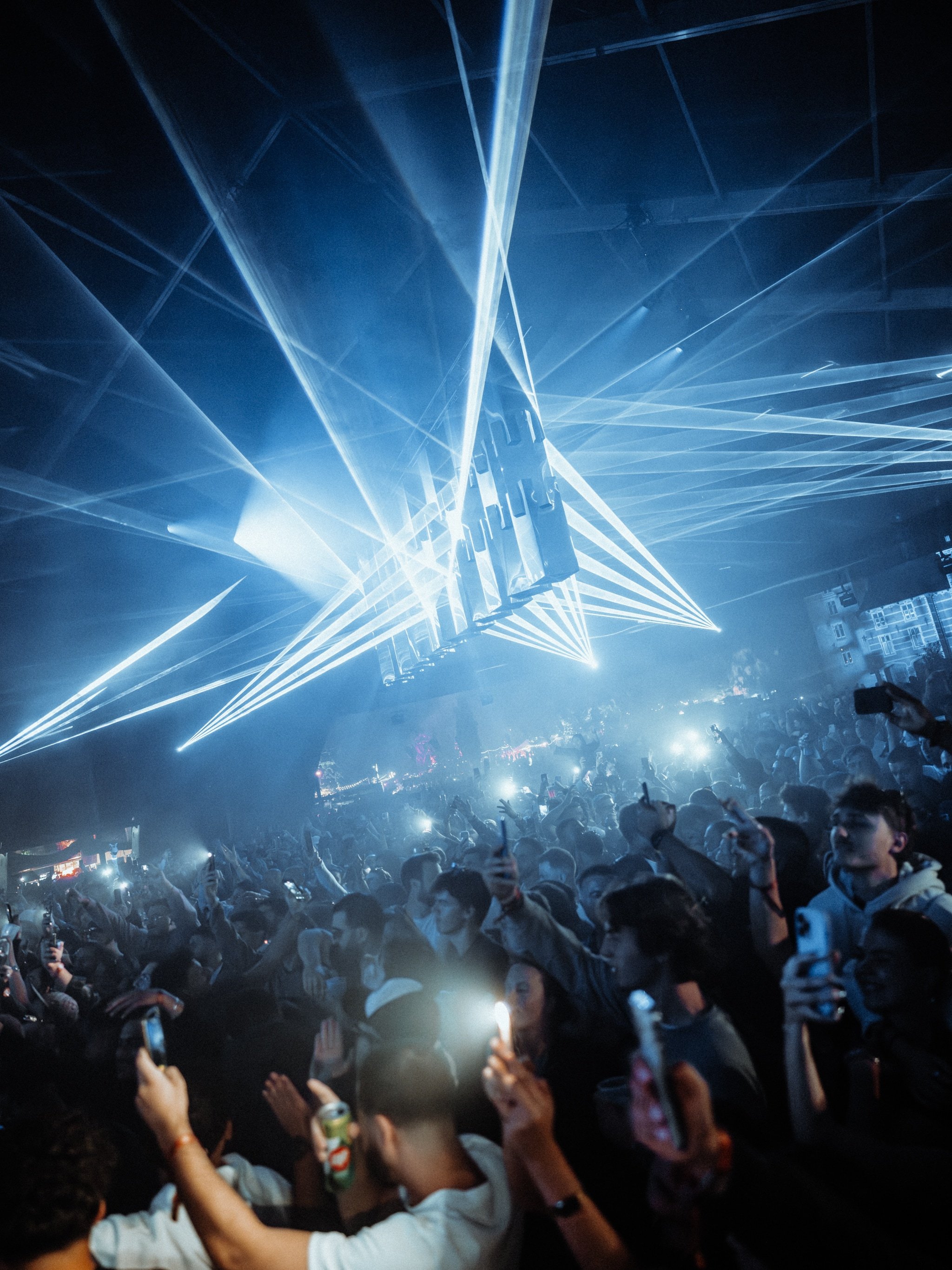 Crowd of people at a concert or nightclub with laser lights projecting across the ceiling. Reflecting Bodies VI Voodoo Village Belgium Scenography art installation light installation Simone Smelt Lumus Instruments Festival main stage