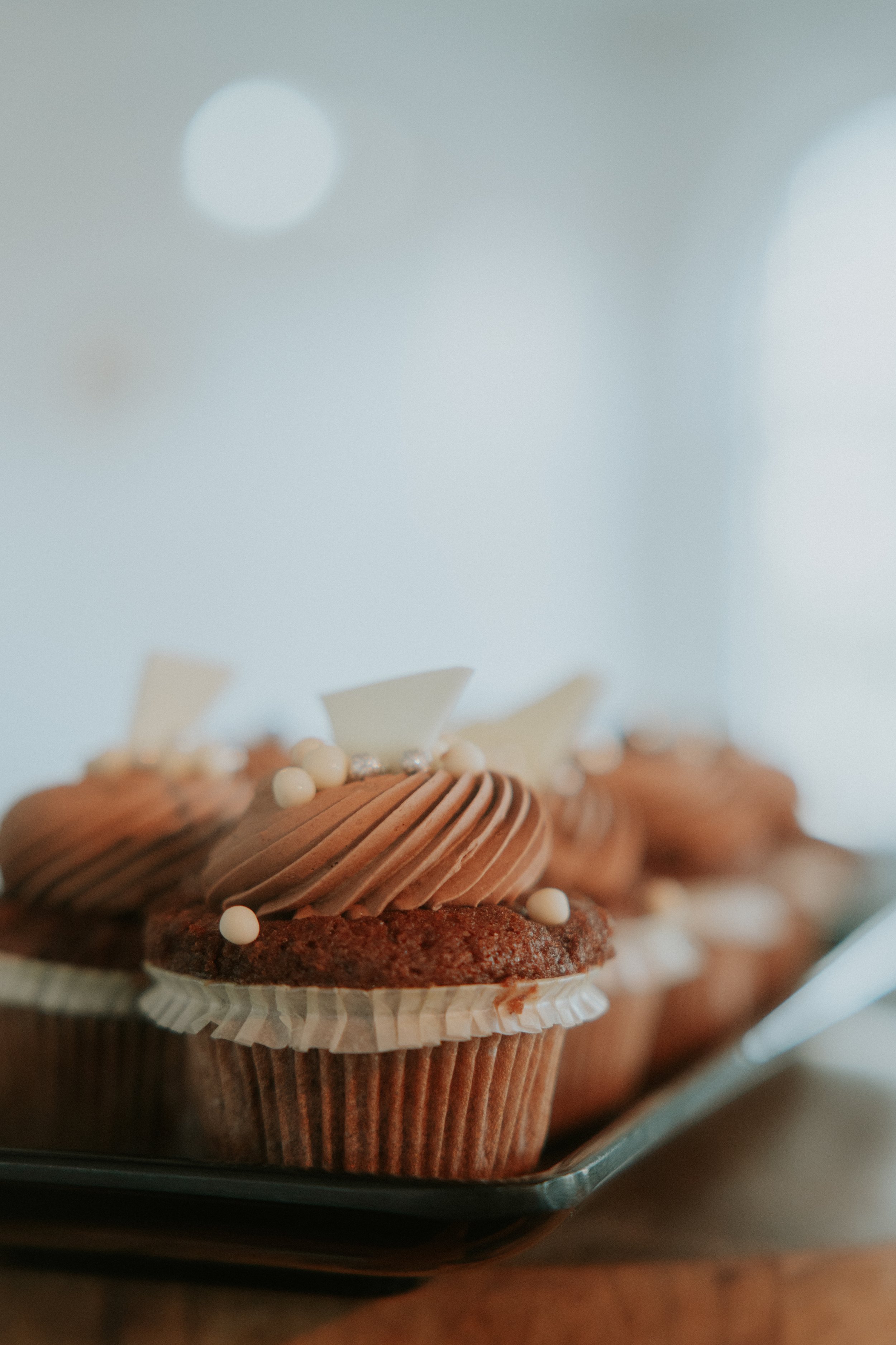 Nahaufnahme von Schokoladen-Cupcakes mit Schokoladencreme und dekorativen Perlen auf einem Tablett.