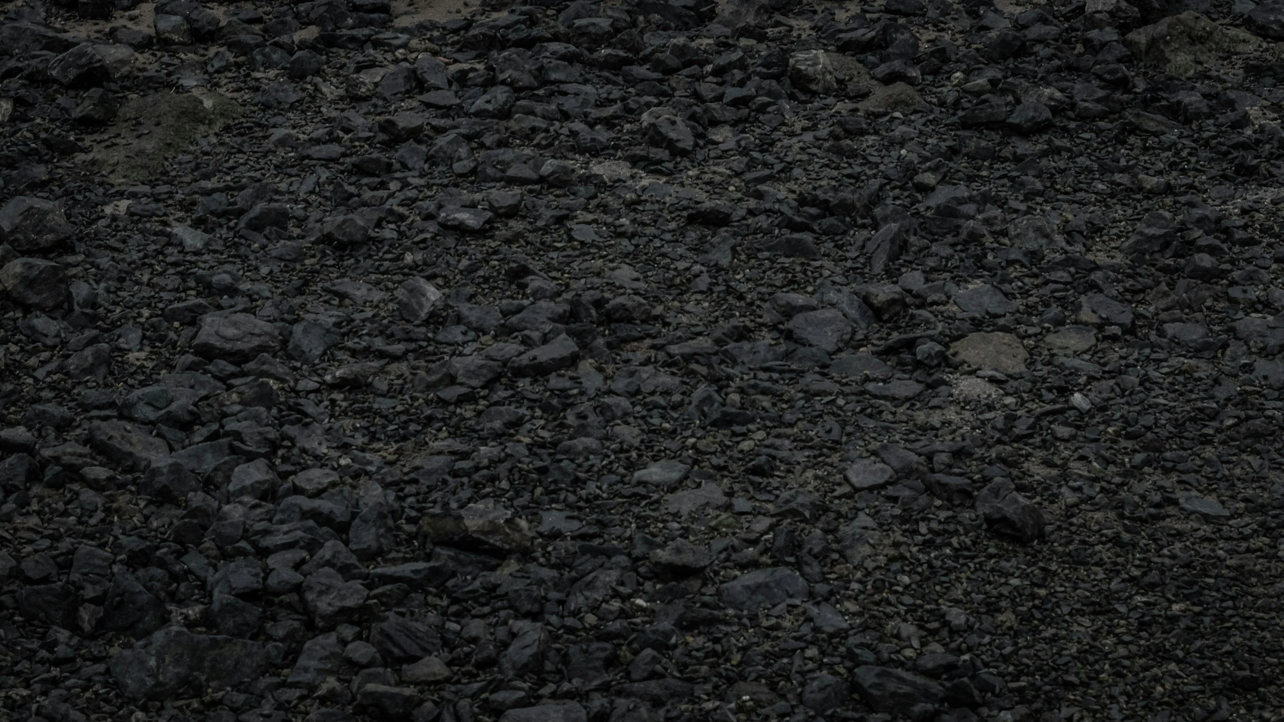 A close-up of a rough, dark, rocky surface with small to medium-sized stones.