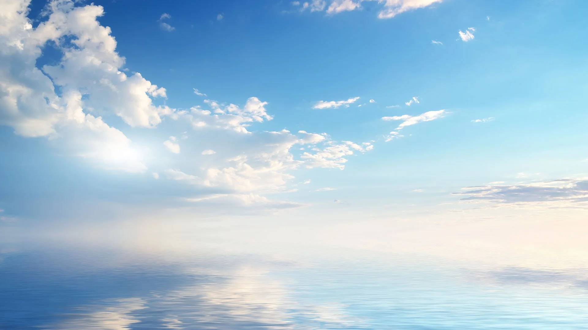 A calm body of water reflecting a partly cloudy blue sky with scattered white clouds.