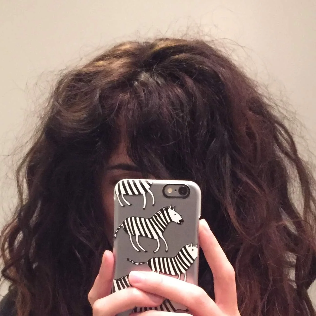 Person with curly hair holding a phone with zebra-patterned case.
