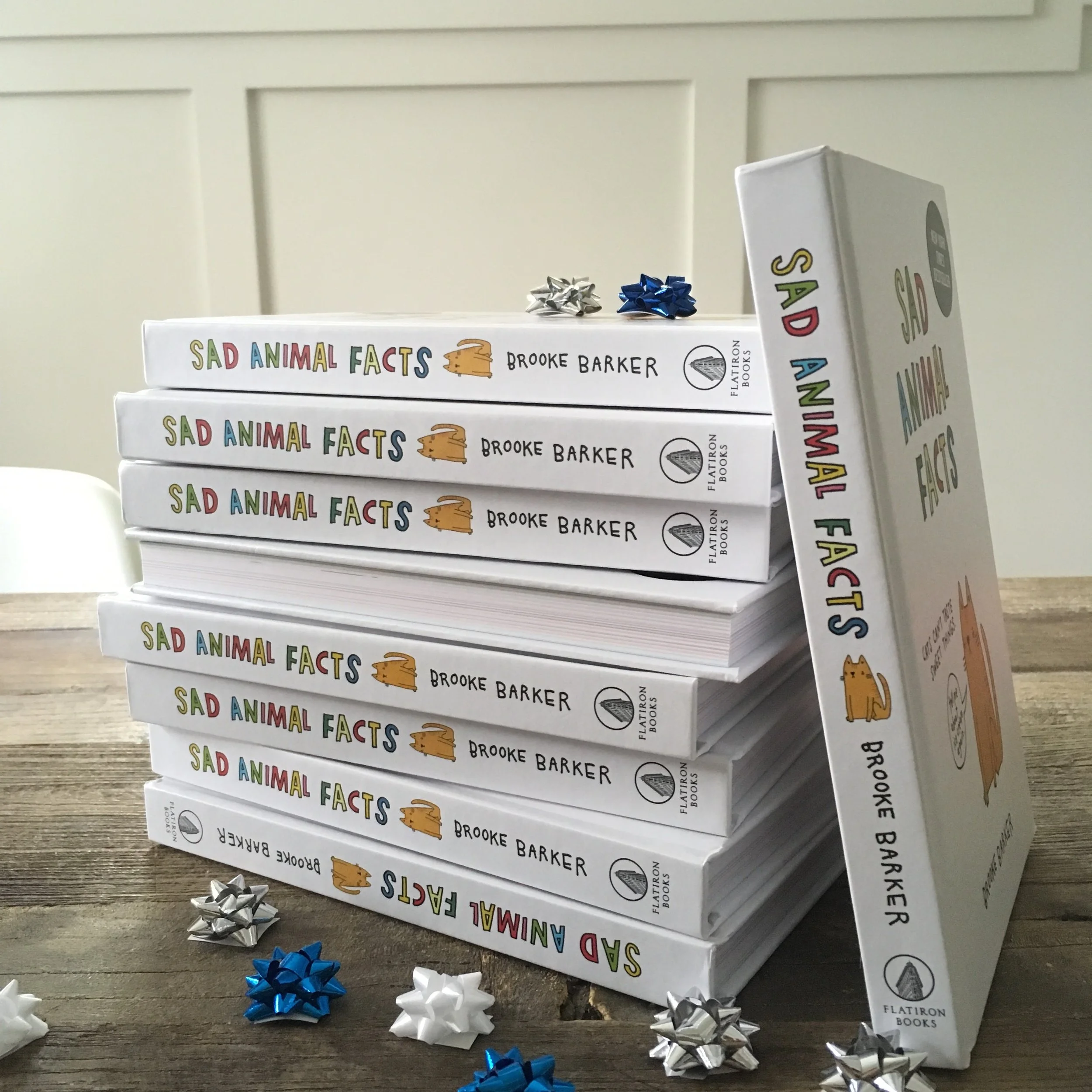 Stack of books titled 'Sad Animal Facts' by Brooke Barker with bows on a wooden surface.