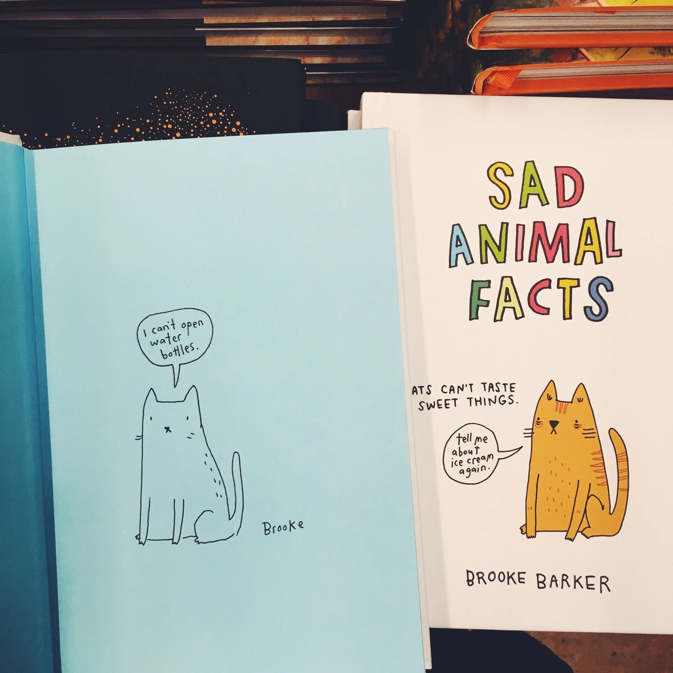 Two books with cartoon cats. The left page shows a blue cat saying "I can't open water bottles." The right book cover is titled "Sad Animal Facts" and depicts a yellow cat with a speech bubble about cats not tasting sweet things.