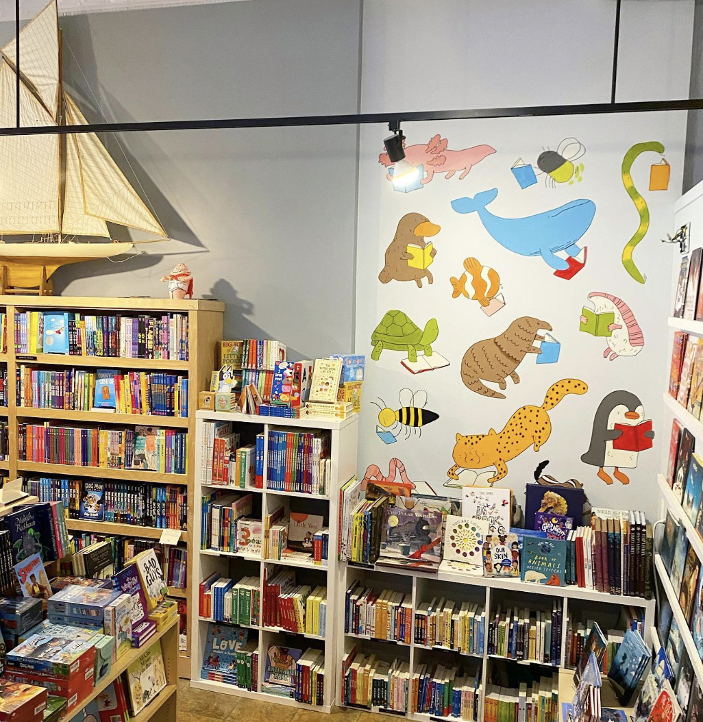 Children's bookstore corner with illustrated animal mural and bookshelves filled with colorful books and toys.