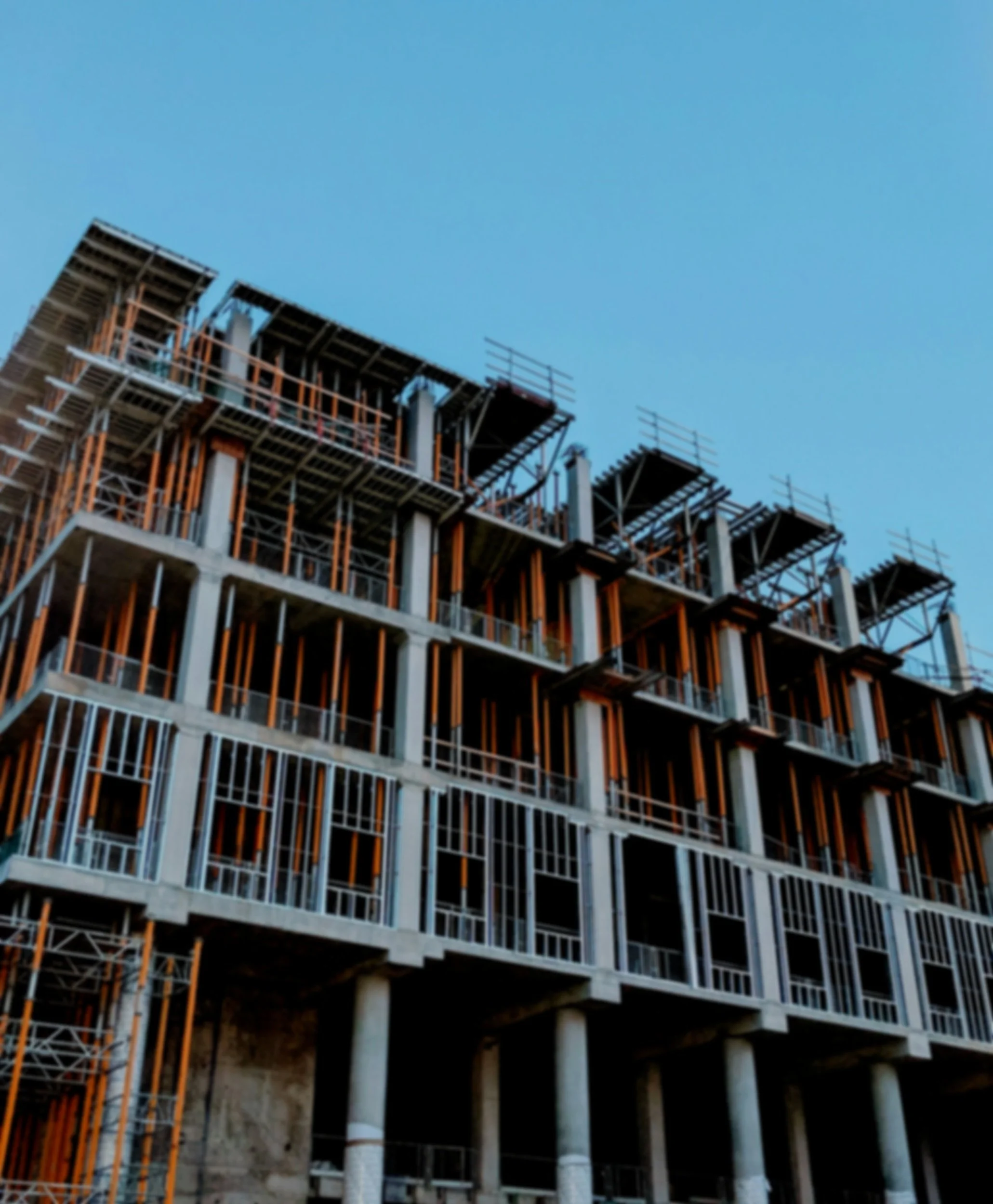 A multi-story building under construction with exposed concrete and scaffolding, against a clear blue sky.