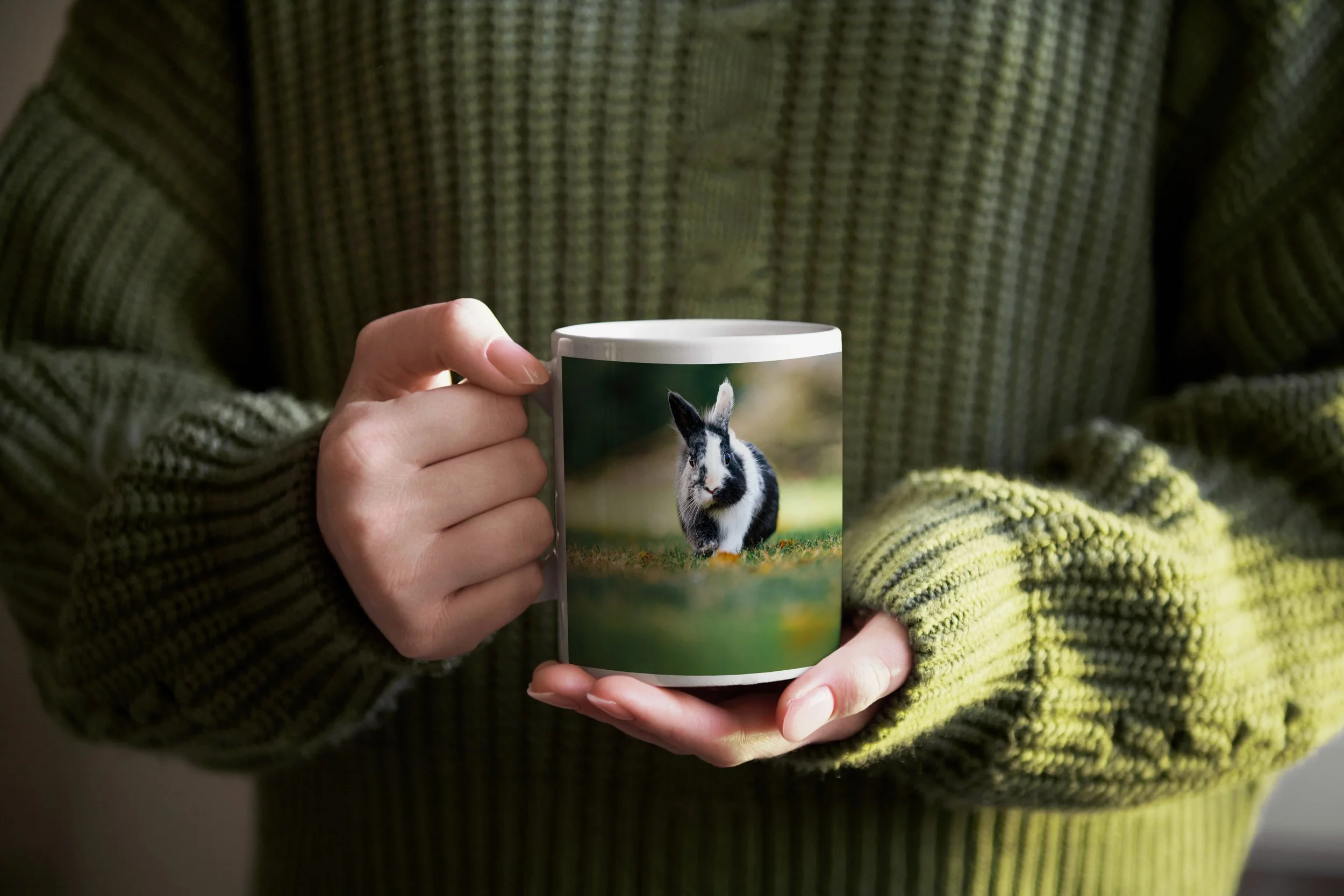 Une personne porte un pull vert à motif, tenant une tasse avec une image d'un lapin