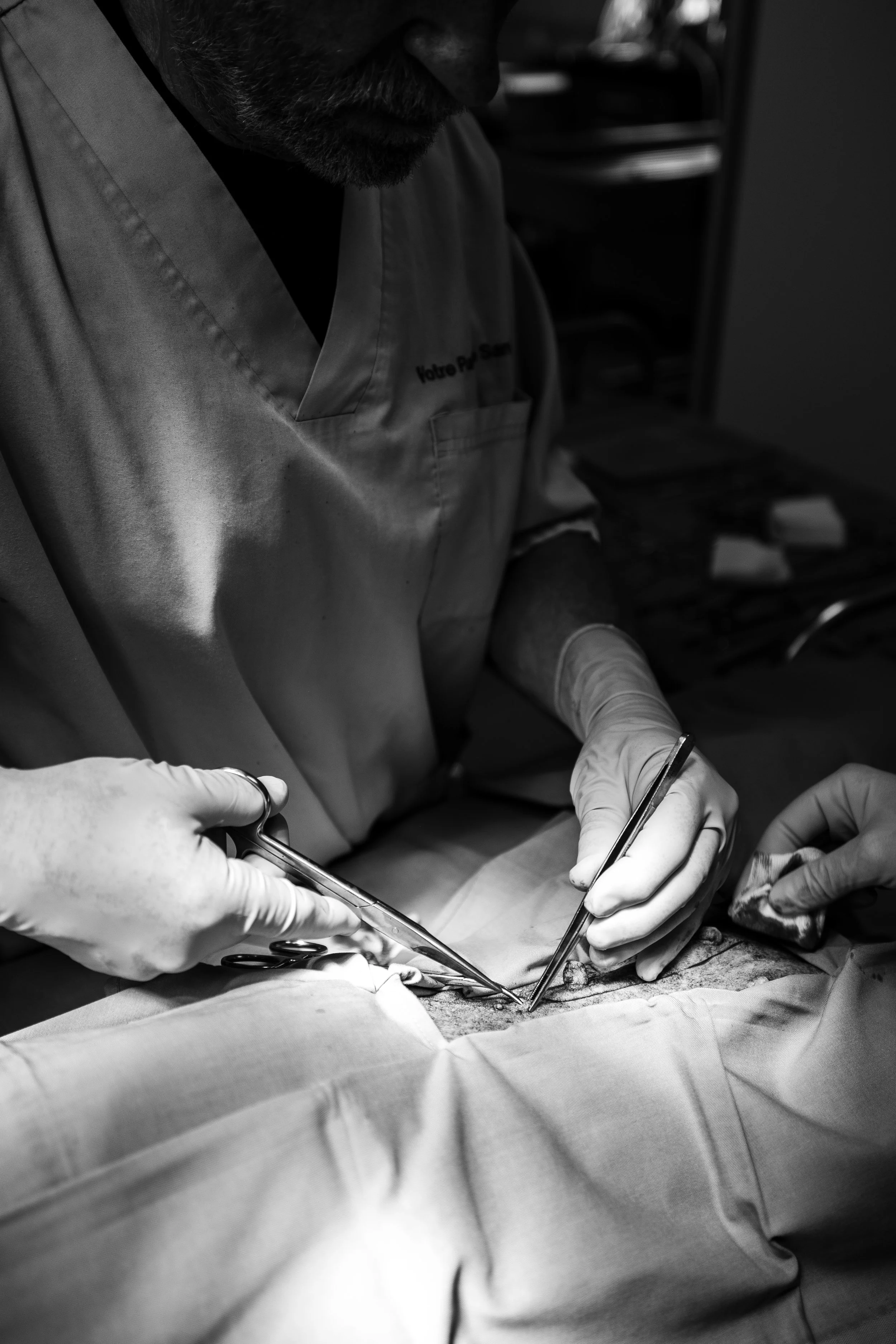 Une opération chirurgicale en cours avec deux mains portant des gants chirurgicaux manipulant des instruments sur un patient, porté par un professionnel en blouse.