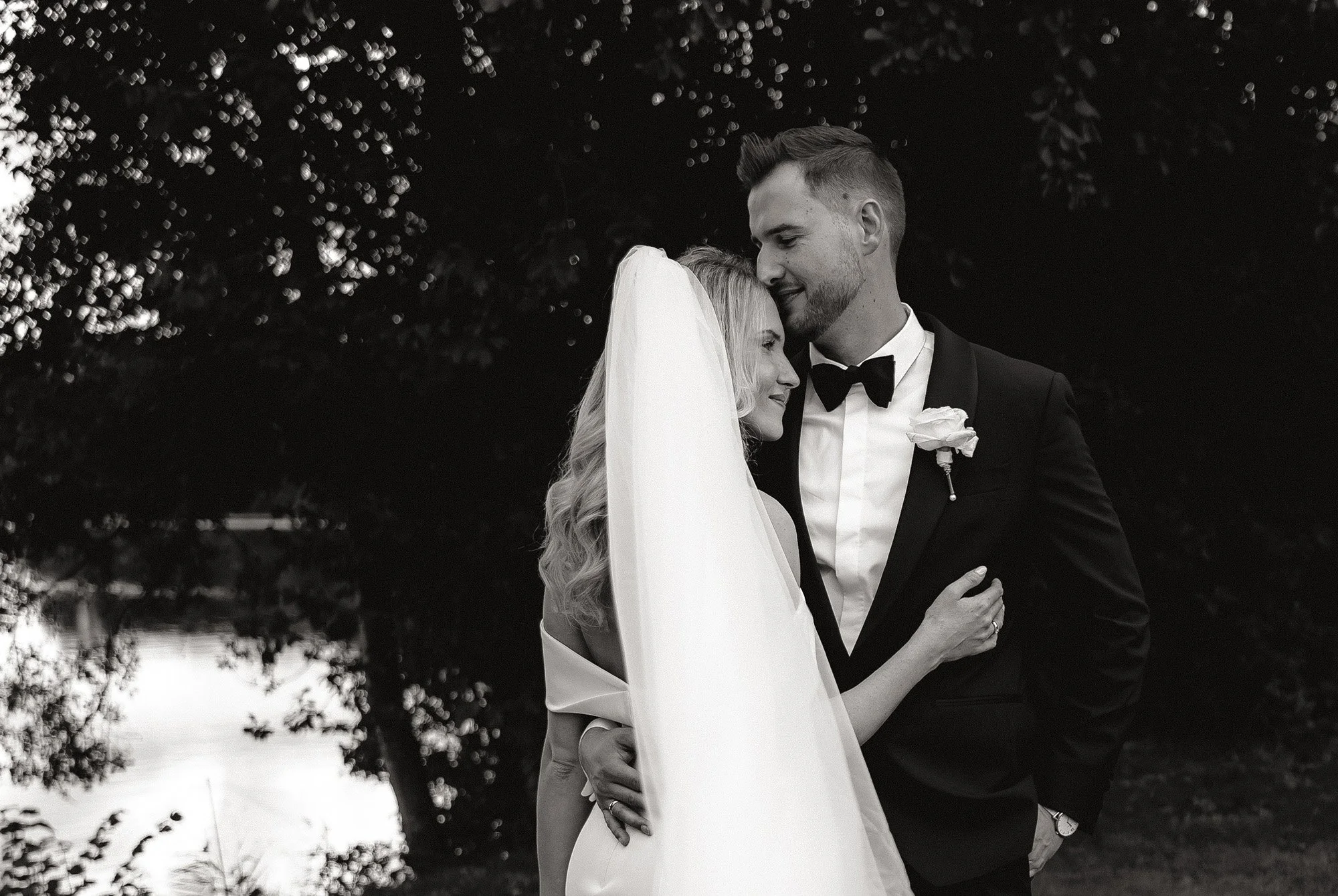 Braut und Bräutigam bei den Paarfotos, in schwarz-weiß. Sie schmiegen sich an einander und der Schleier weht im Wind.