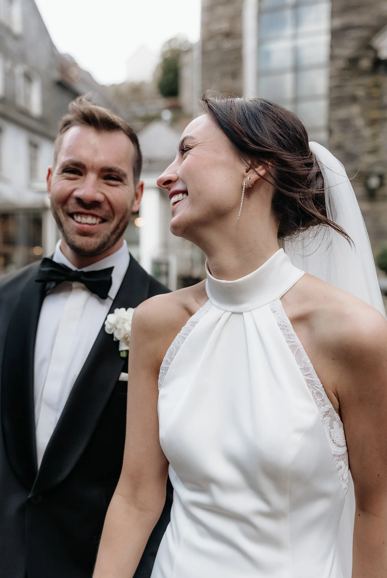 Ein lachendes Brautpaar draußen vor einem historischen Gebäude.