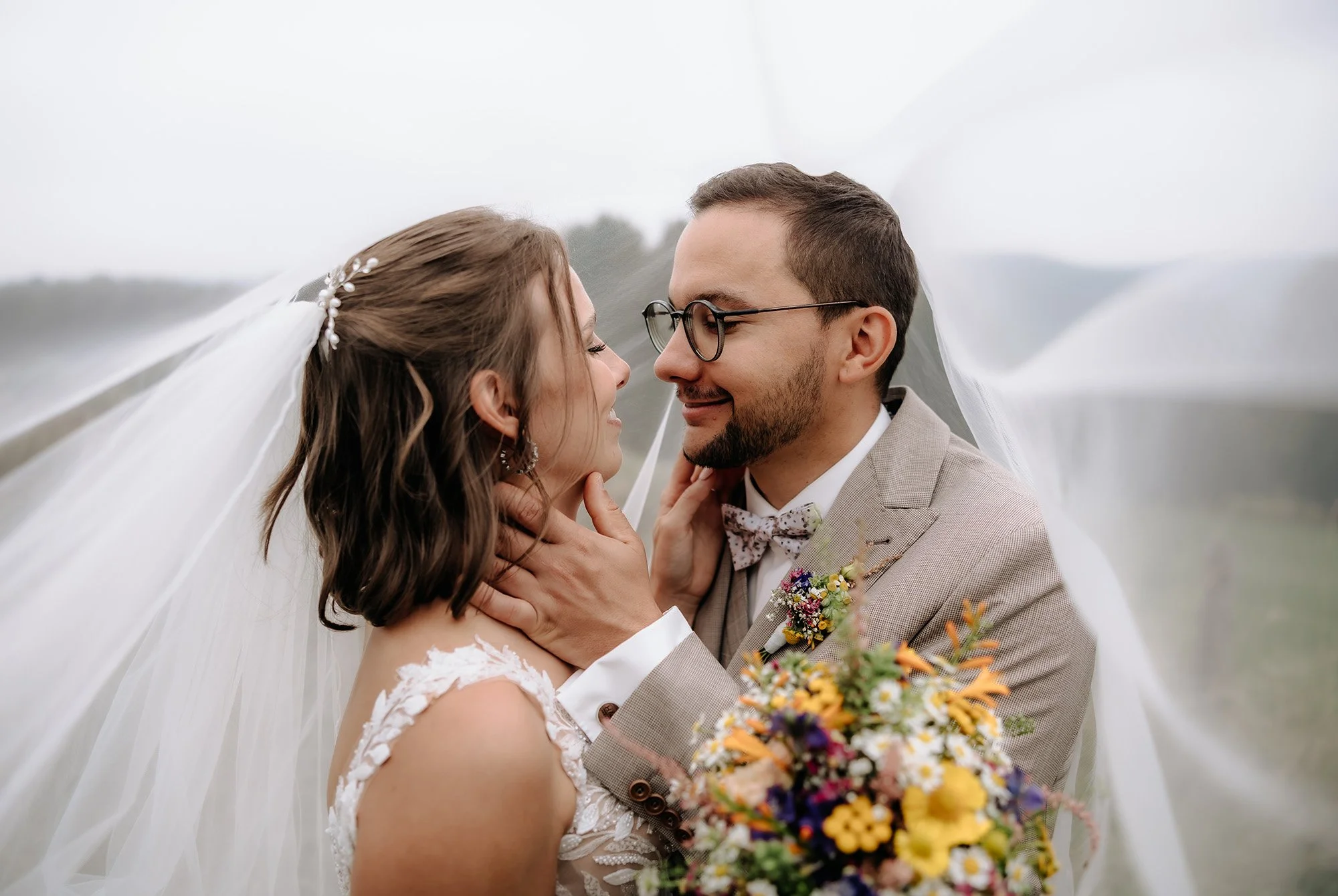 Braut und Bräutigam unter dem Schleier, der Brautstrauß mit bunten Sommerblumen im Vordergrund.
