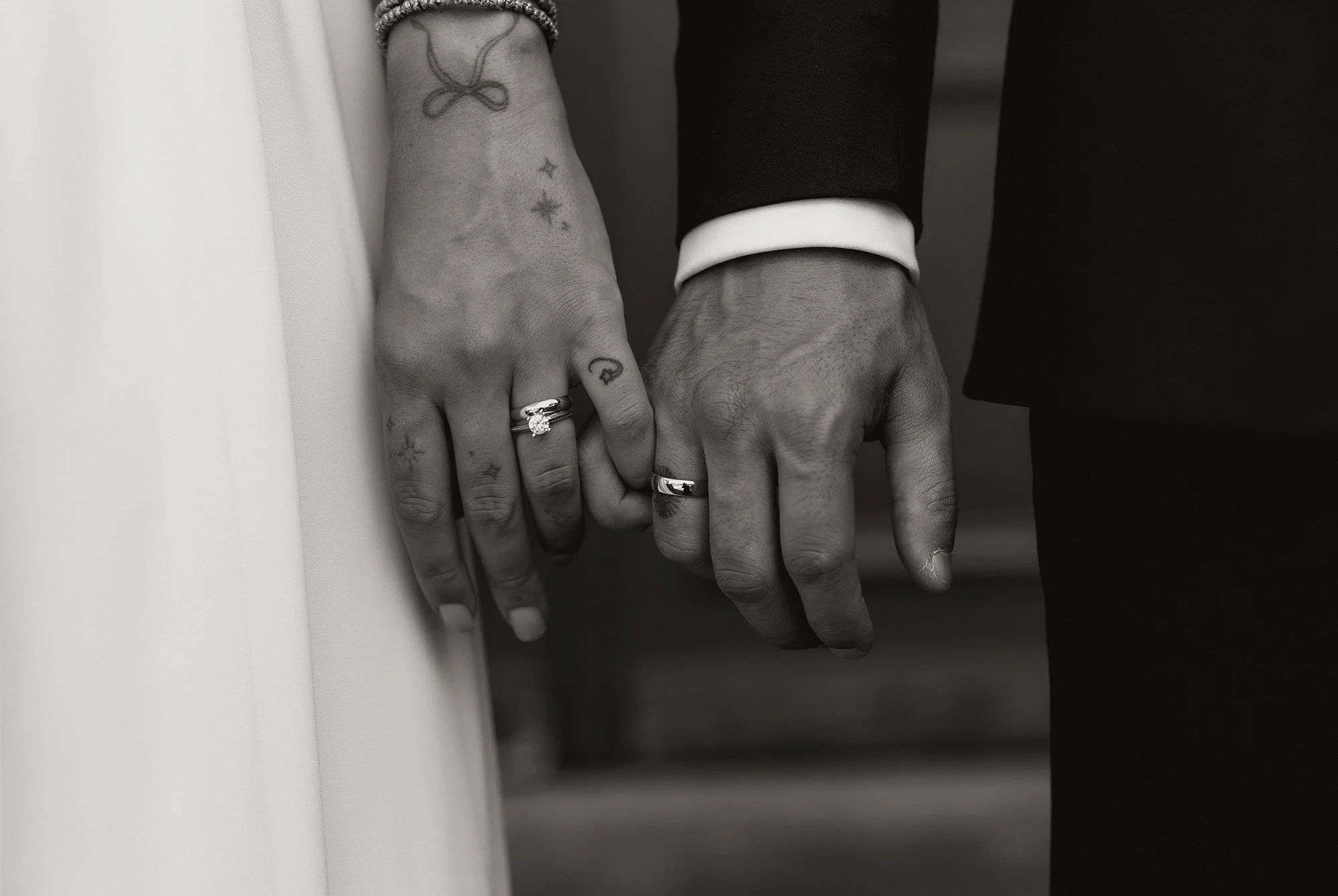 Schwarz-weiße Detailaufnahme der Hände von Braut und Bräutigam mit Fokus auf die Eheringe