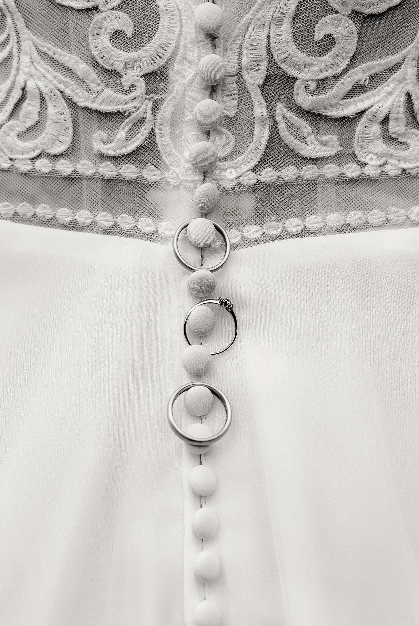 Detailaufnahme der Eheringe, wie sie an der Knopfleiste des Brautkleides hängen.