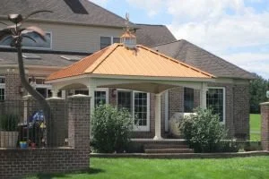 Back view of a house with a covered patio, brick pillars, large windows, and a green lawn.