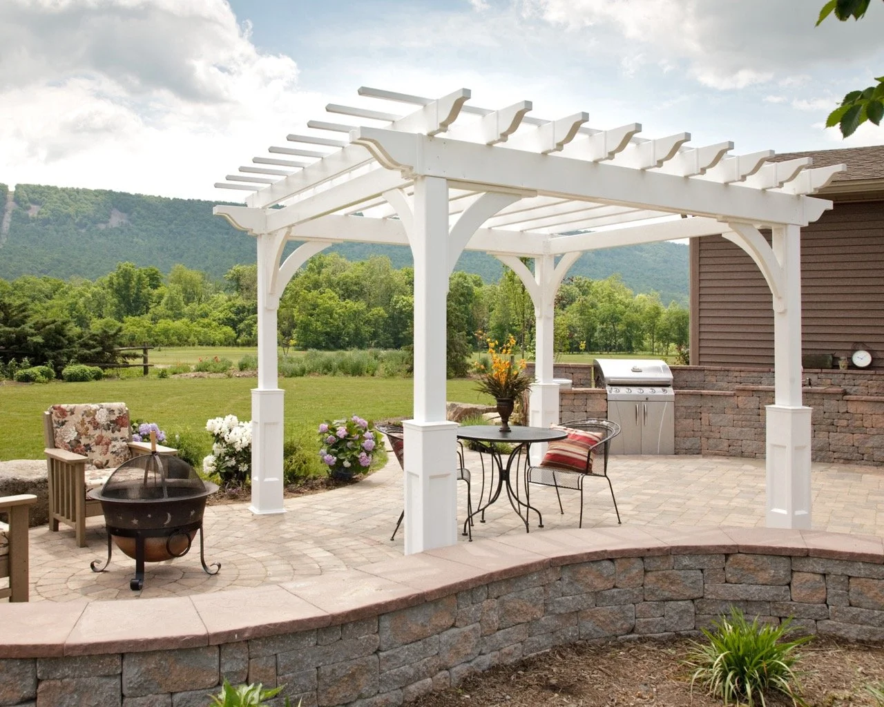 Outdoor patio with white pergola, seating area, barbecue grill, garden, and scenic mountain view.