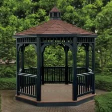 A black wooden gazebo with a brown roof in a park with green trees